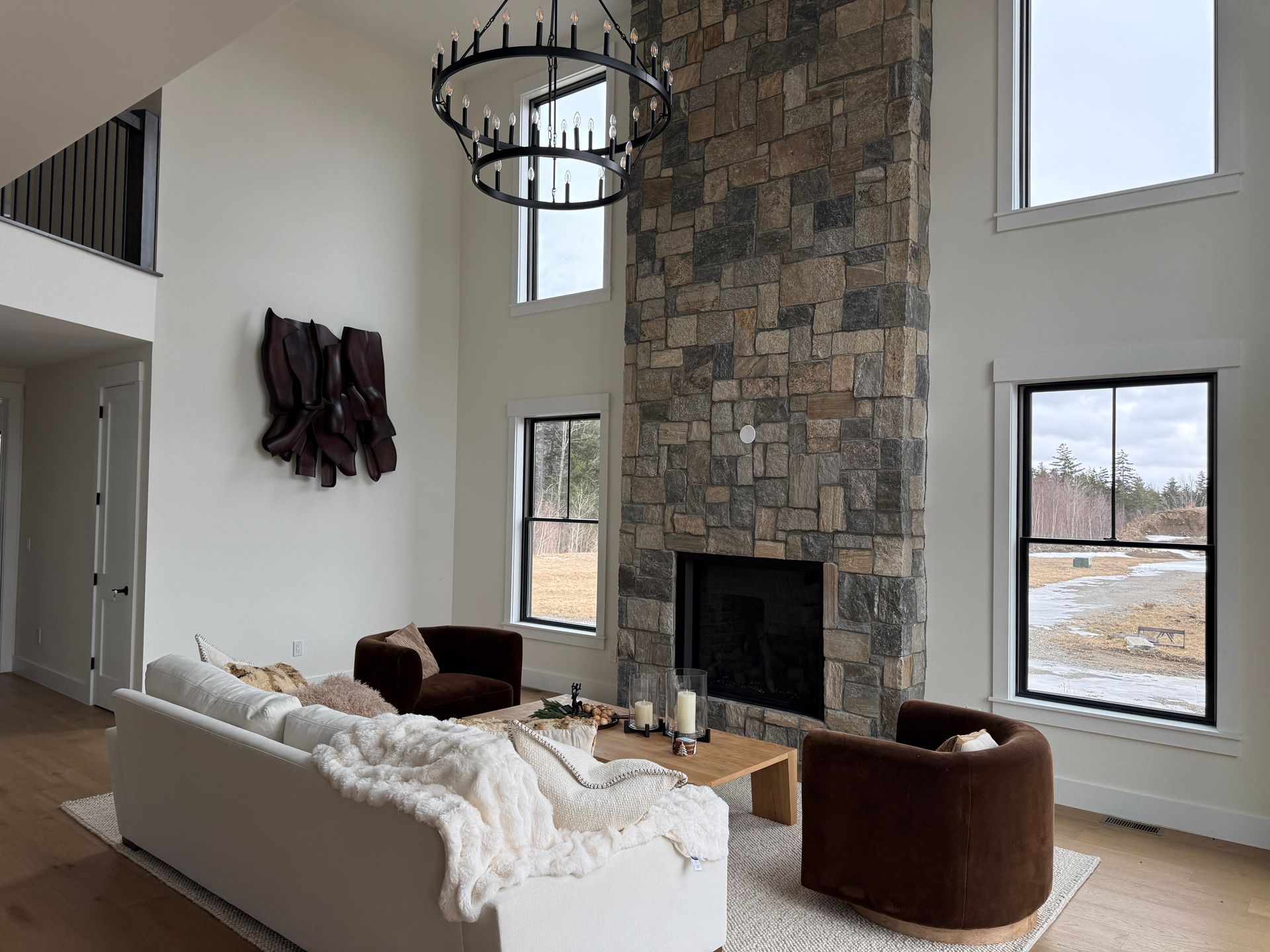 A bright, modern living room with a tall stone fireplace, white walls, a white sofa, and two brown swivel chairs.