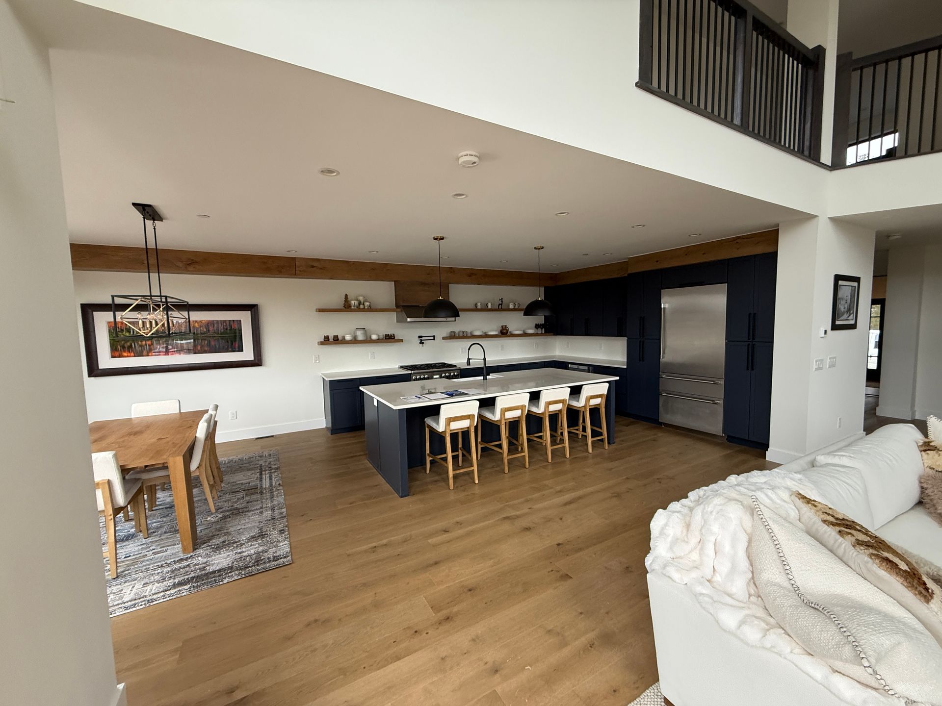 An open-concept kitchen and dining area featuring dark blue cabinetry, a large island with stools, and wooden beams.