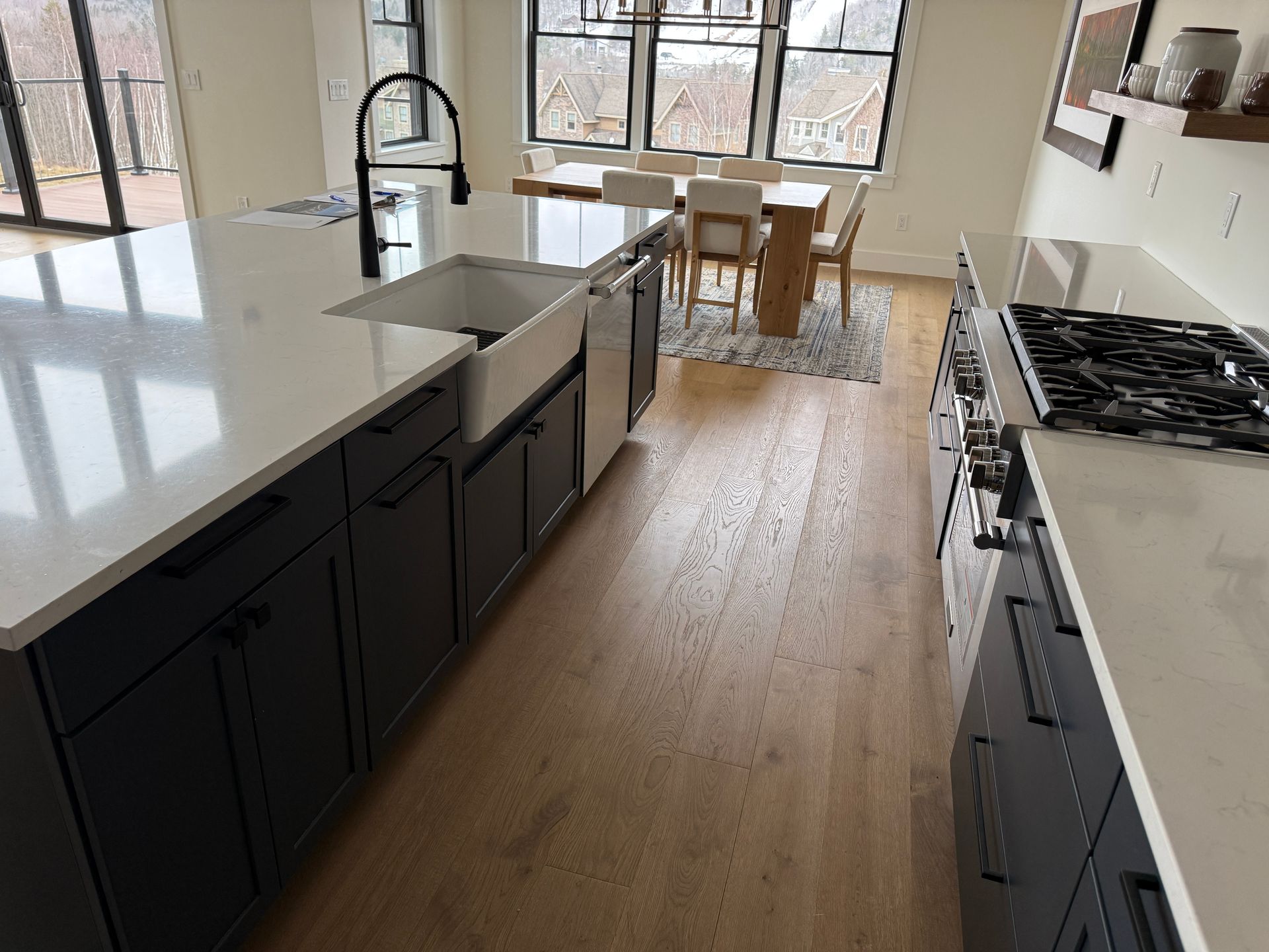 Modern kitchen with a dark-cabinet island, white quartz countertops, a farmhouse sink, and light hardwood floors.