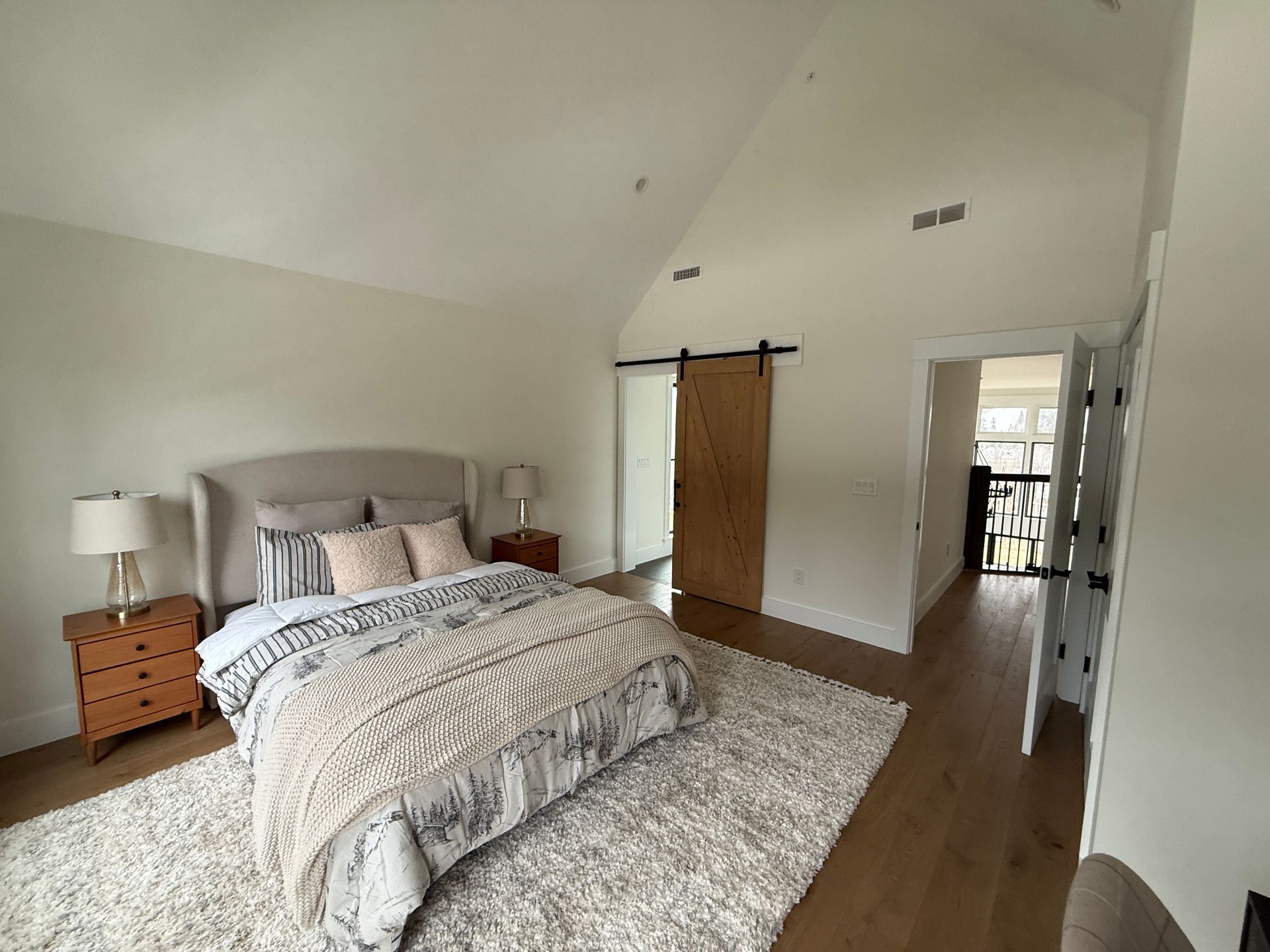 Bright bedroom with a vaulted ceiling, a bed with patterned bedding, a textured rug, and a rustic wooden barn door.