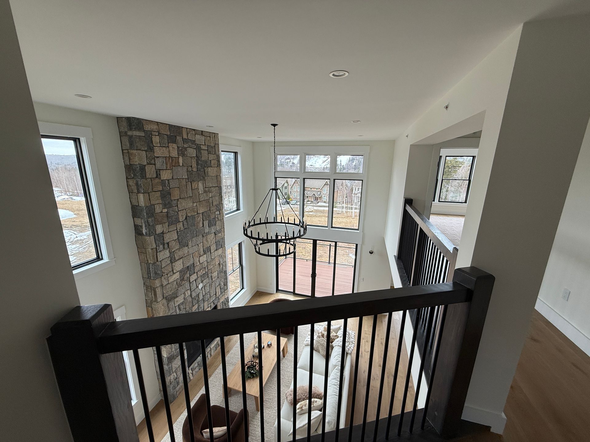 A high-angle view of a modern living room with a large stone fireplace, chandelier, floor-to-ceiling windows, and balcony.