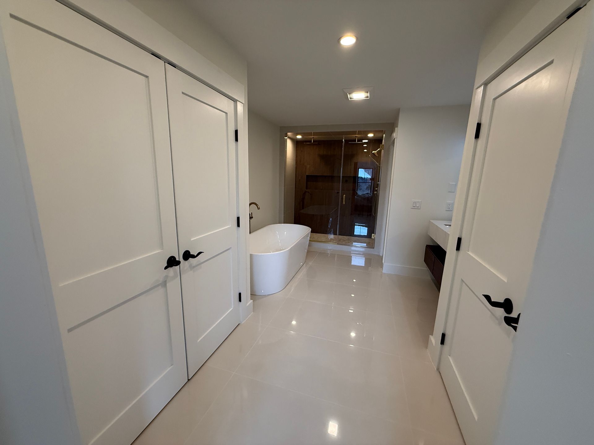 A white-walled bathroom features a freestanding tub, a walk-in glass shower, and a vanity, with light tile flooring.