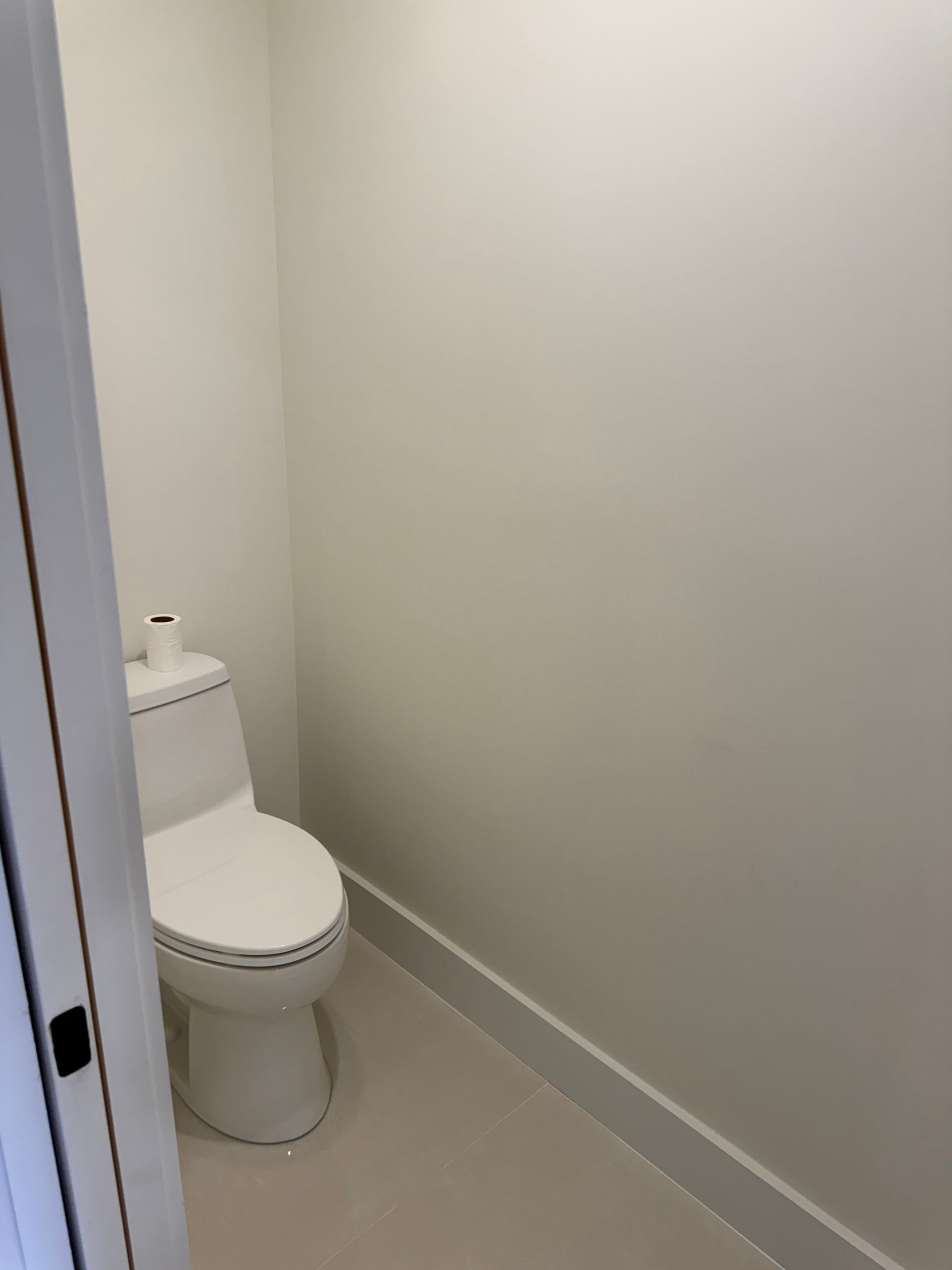 A white toilet sits in a small, minimalist bathroom with white walls and flooring, viewed from the doorway.