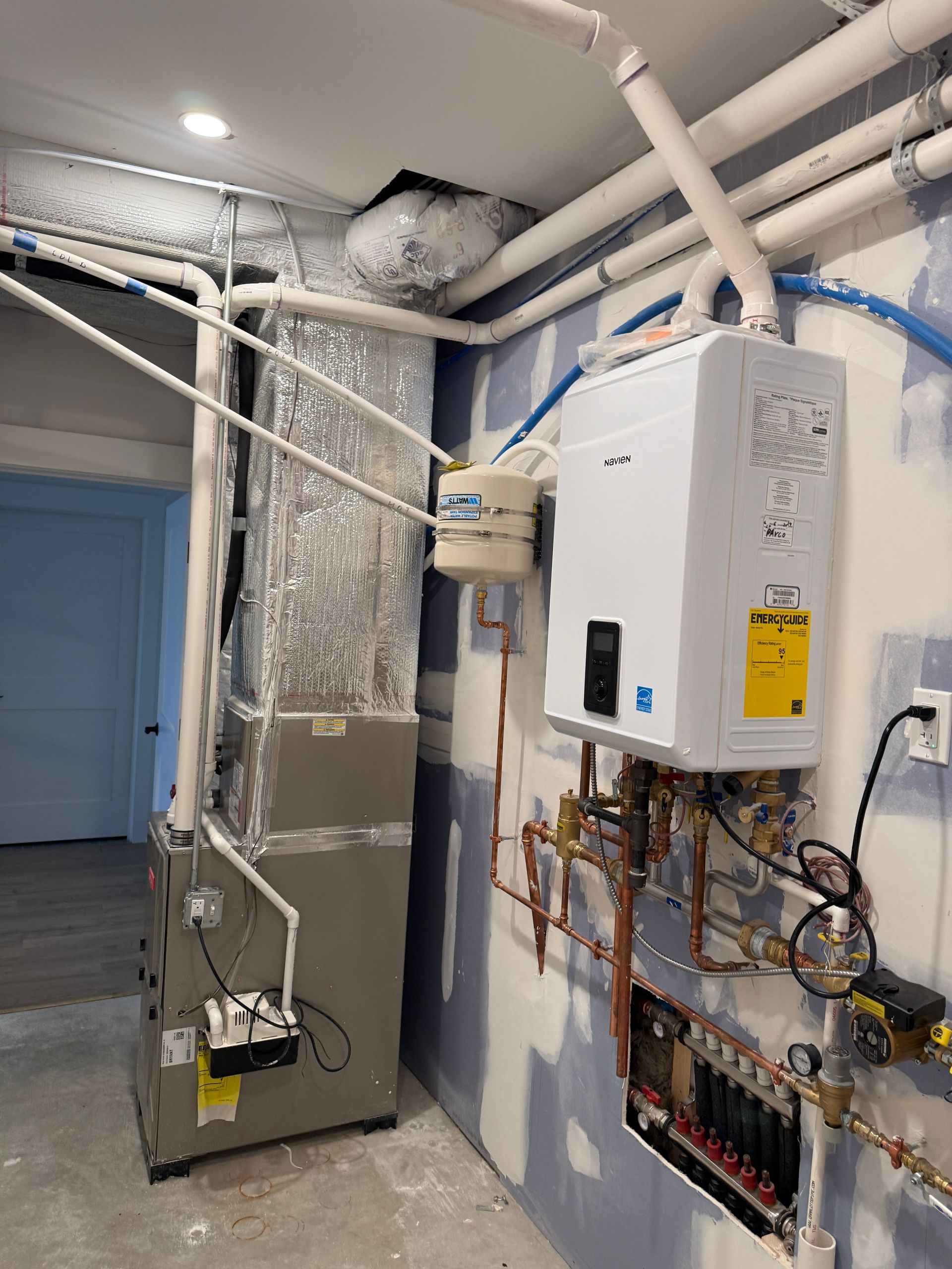 Utility room with a white tankless water heater, copper piping, and a grey HVAC furnace unit against a painted wall.