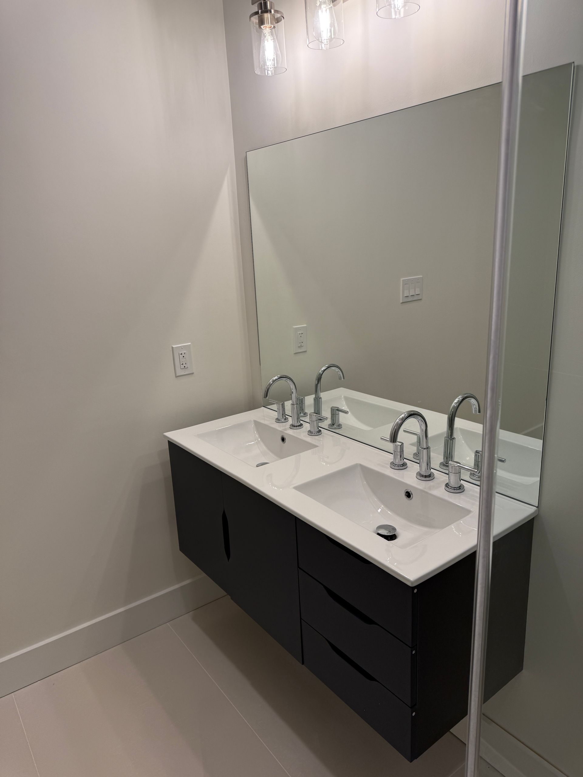 A floating double-sink bathroom vanity with dark cabinets, white countertops, chrome faucets, and a large wall mirror.