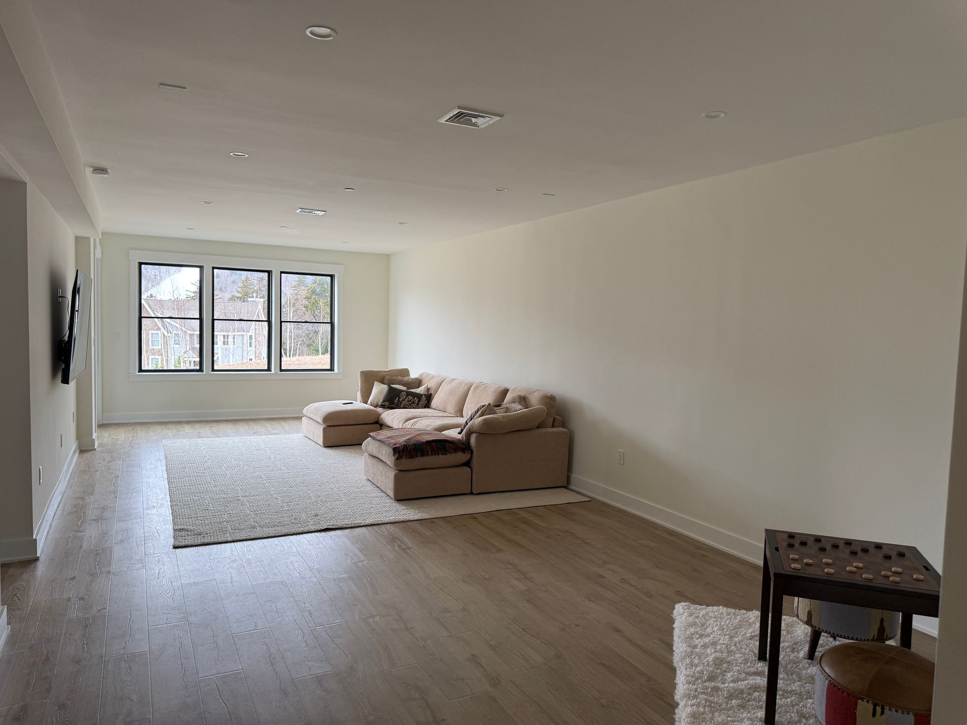 A beige sectional sofa sits on a textured rug in a spacious, light-filled living room with white walls and wood floors.