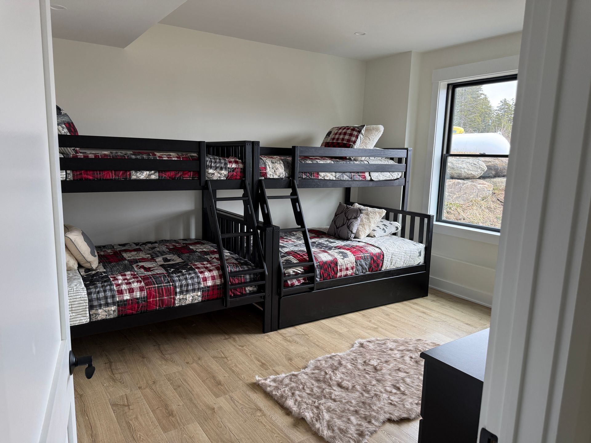 Two dark wood bunk beds with plaid bedding sit in a bedroom with light wood floors and a window.