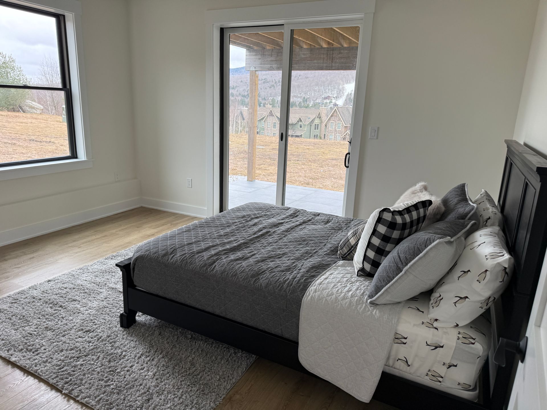 A modern bedroom with a black bed frame, gray bedding, and a shag rug, featuring a large window and glass sliding door.