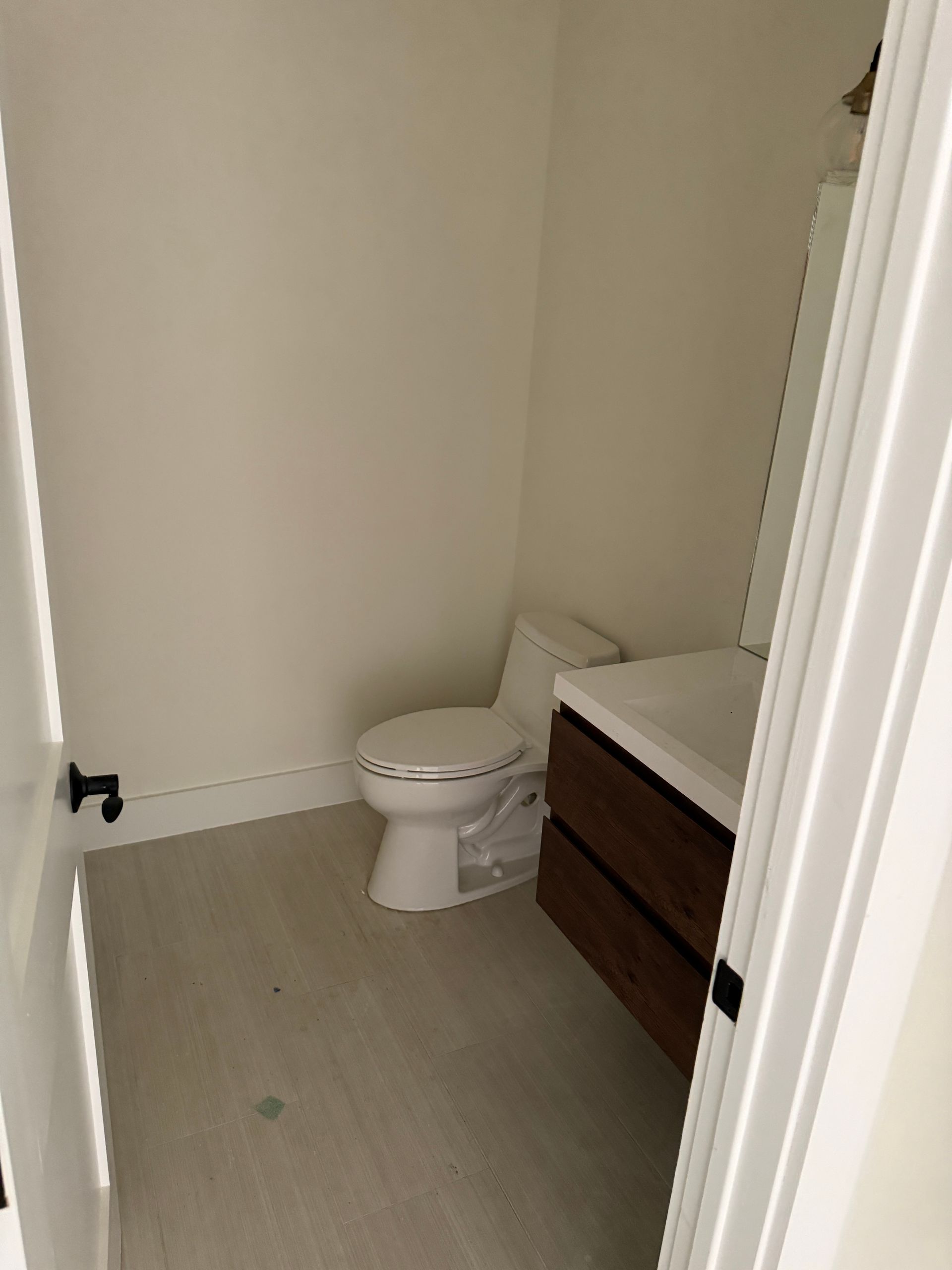 A small, neutral-toned half bathroom with a white toilet and a modern dark wood floating vanity.