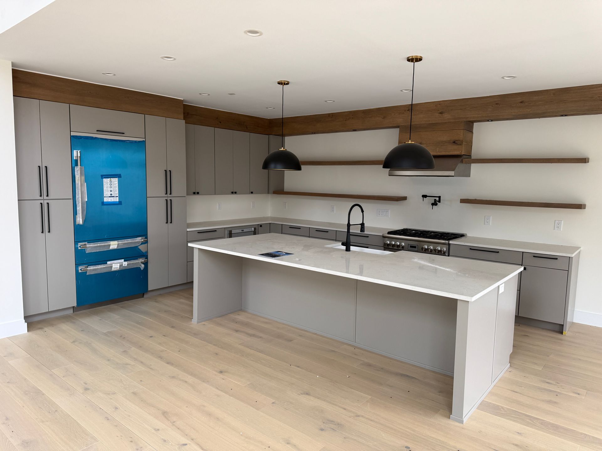 Modern kitchen with light gray cabinets, a bright blue refrigerator, a white kitchen island, and natural wood shelving.