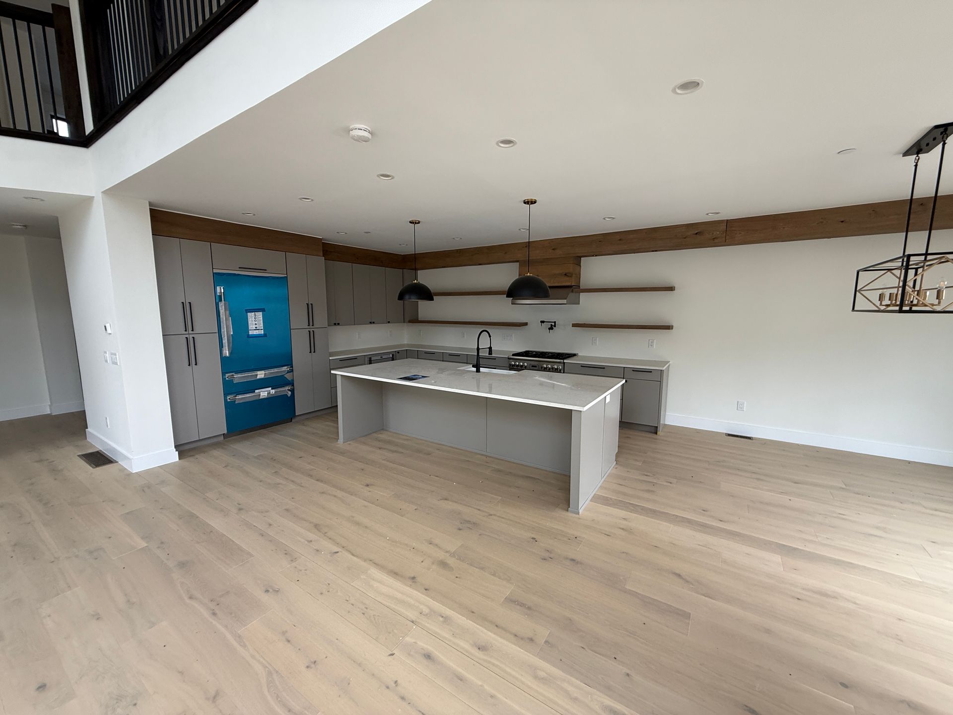 A modern open-concept kitchen with light wood floors, gray cabinetry, a central island, and blue-taped appliances.
