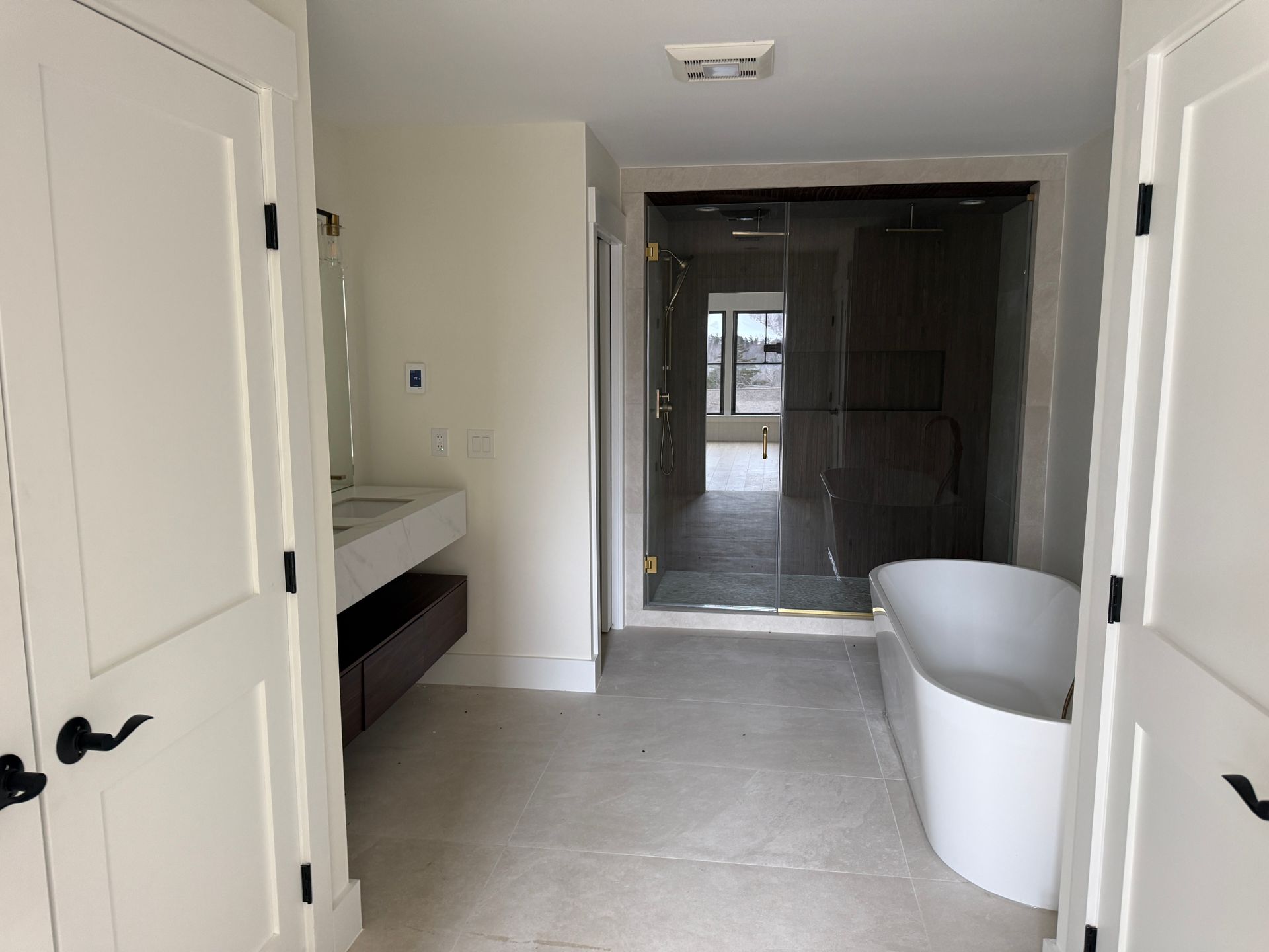 A modern bathroom with white double doors, a floating wood vanity, a standalone soaking tub, and a large glass shower.