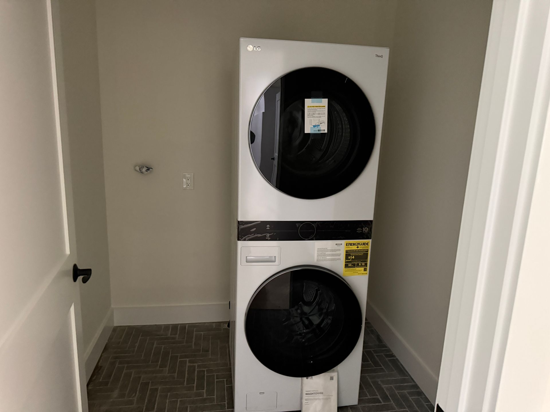A new white stacked washer and dryer unit in a small laundry closet with a herringbone-patterned floor.