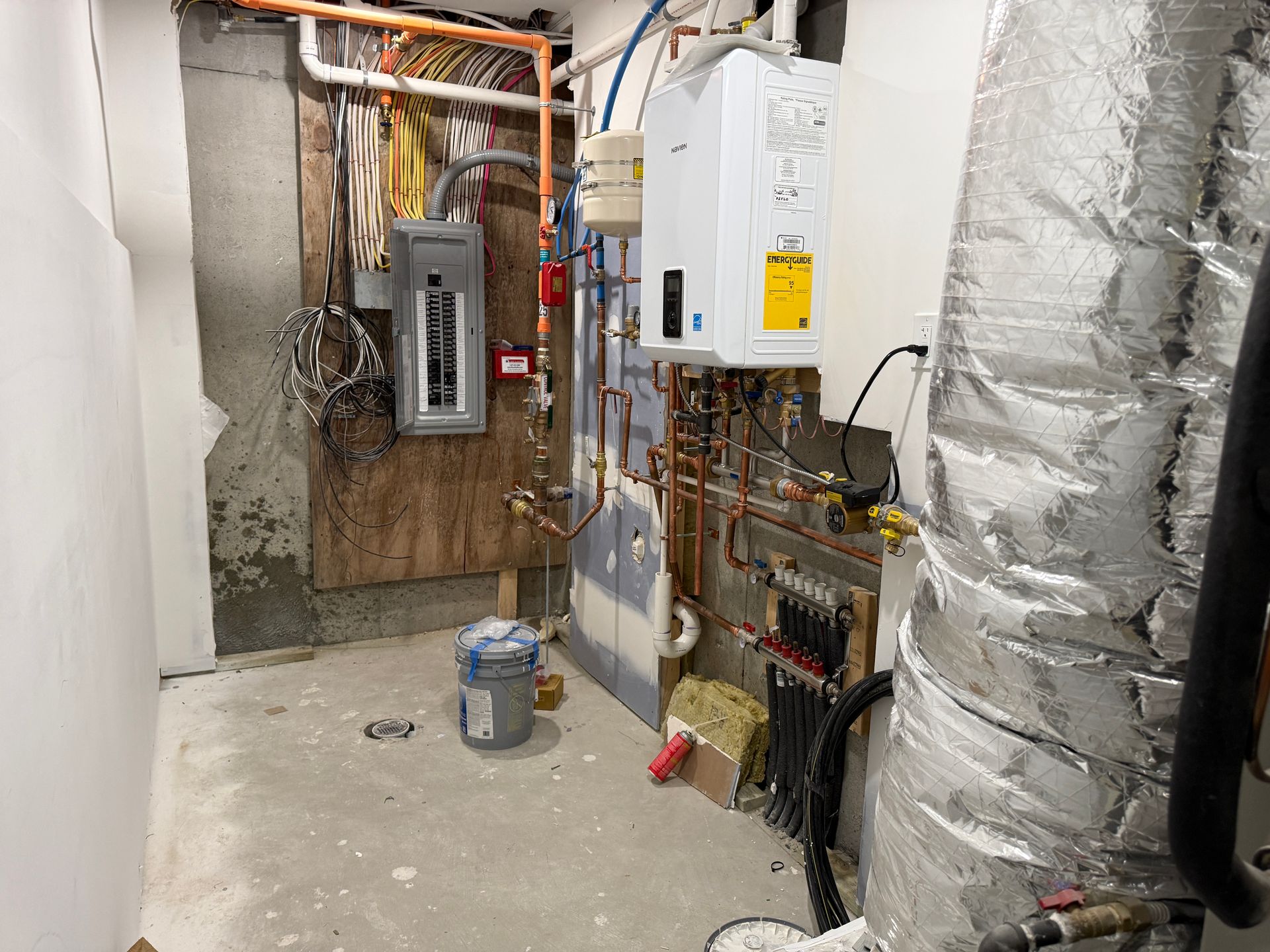 Mechanical utility room featuring a wall-mounted tankless water heater, electrical panel, plumbing, and ductwork.