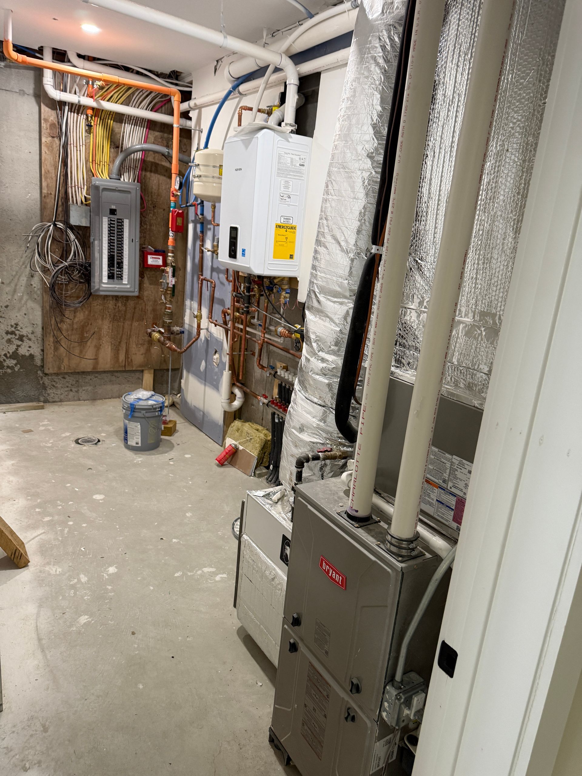A utility room featuring a furnace, a tankless water heater, copper piping, an electrical panel, and exposed ductwork.