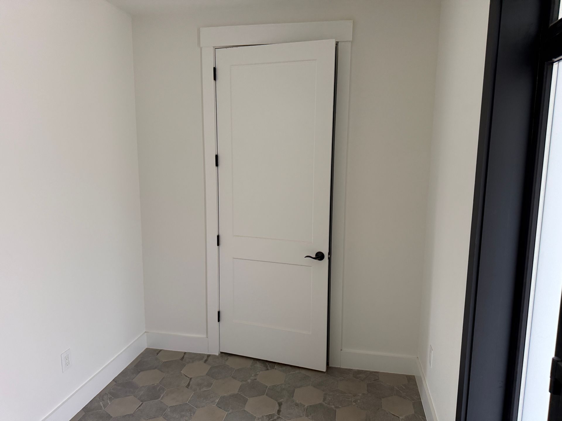 A white door with black hinges and handle set against light walls in a room with hexagon-patterned floor tiles.
