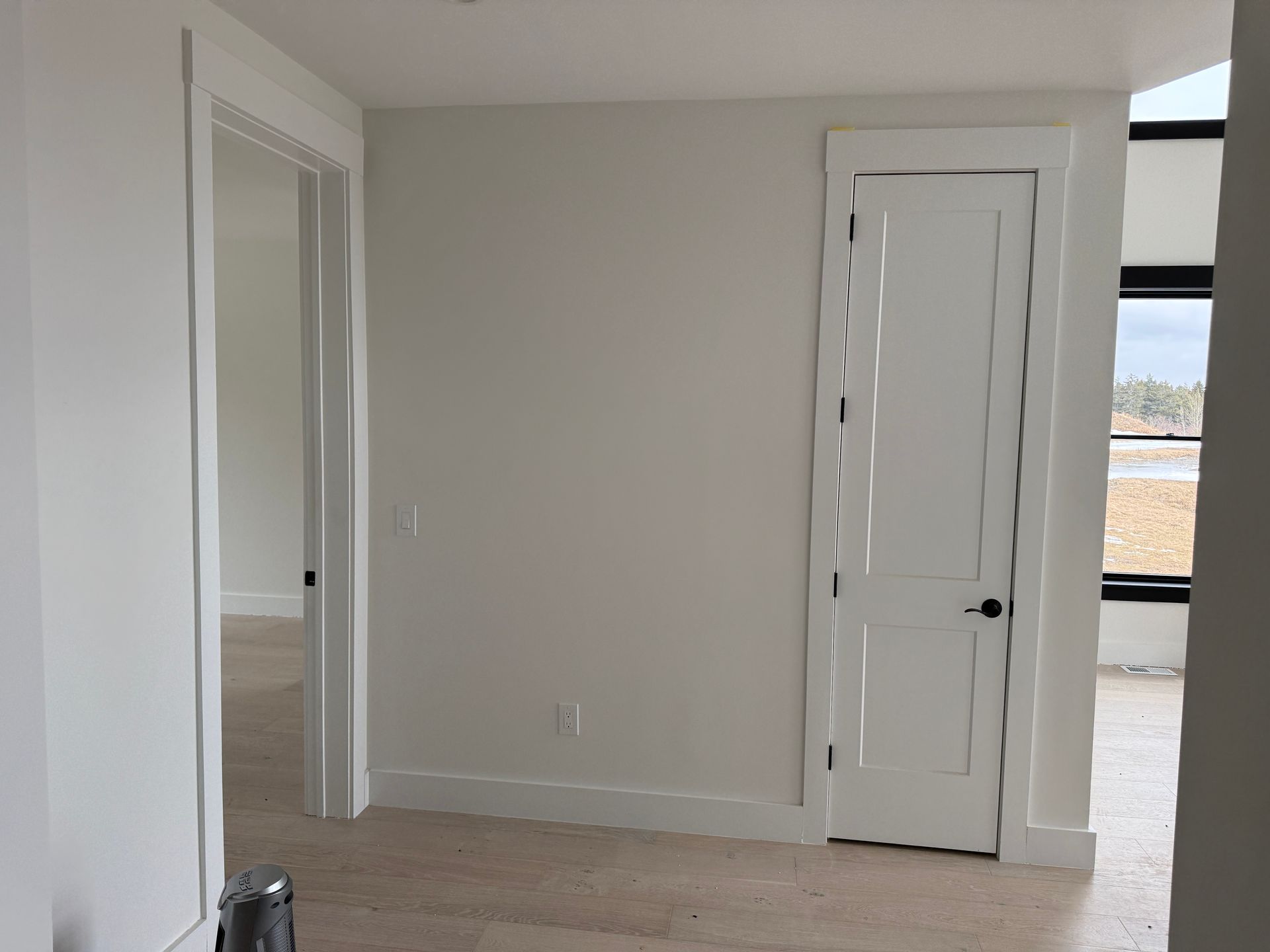A room interior featuring a beige wall, a white door, a doorway leading to another room, and light-colored flooring.