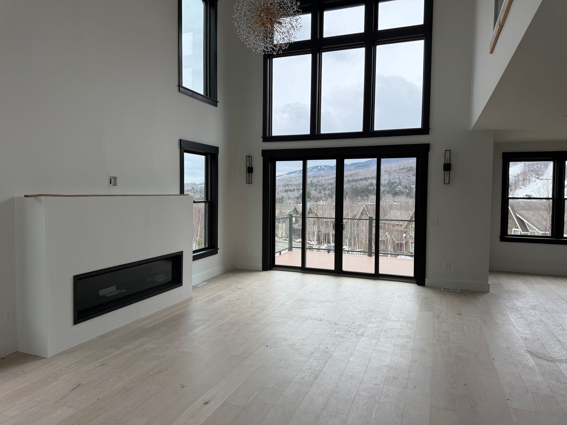 Modern living room with a minimalist fireplace, light wood floors, and floor-to-ceiling windows.
