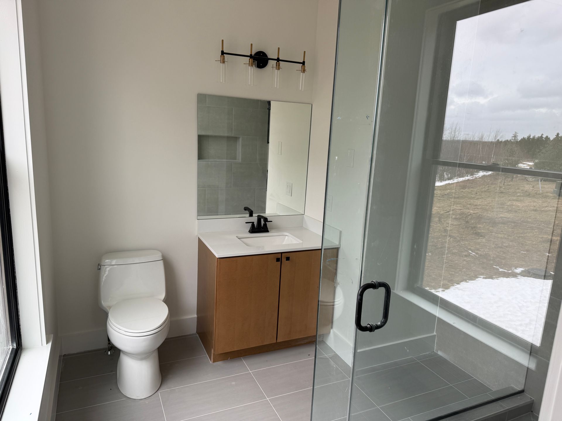 A modern bathroom featuring a white toilet, a light wood vanity with a black faucet, and a glass-enclosed shower.