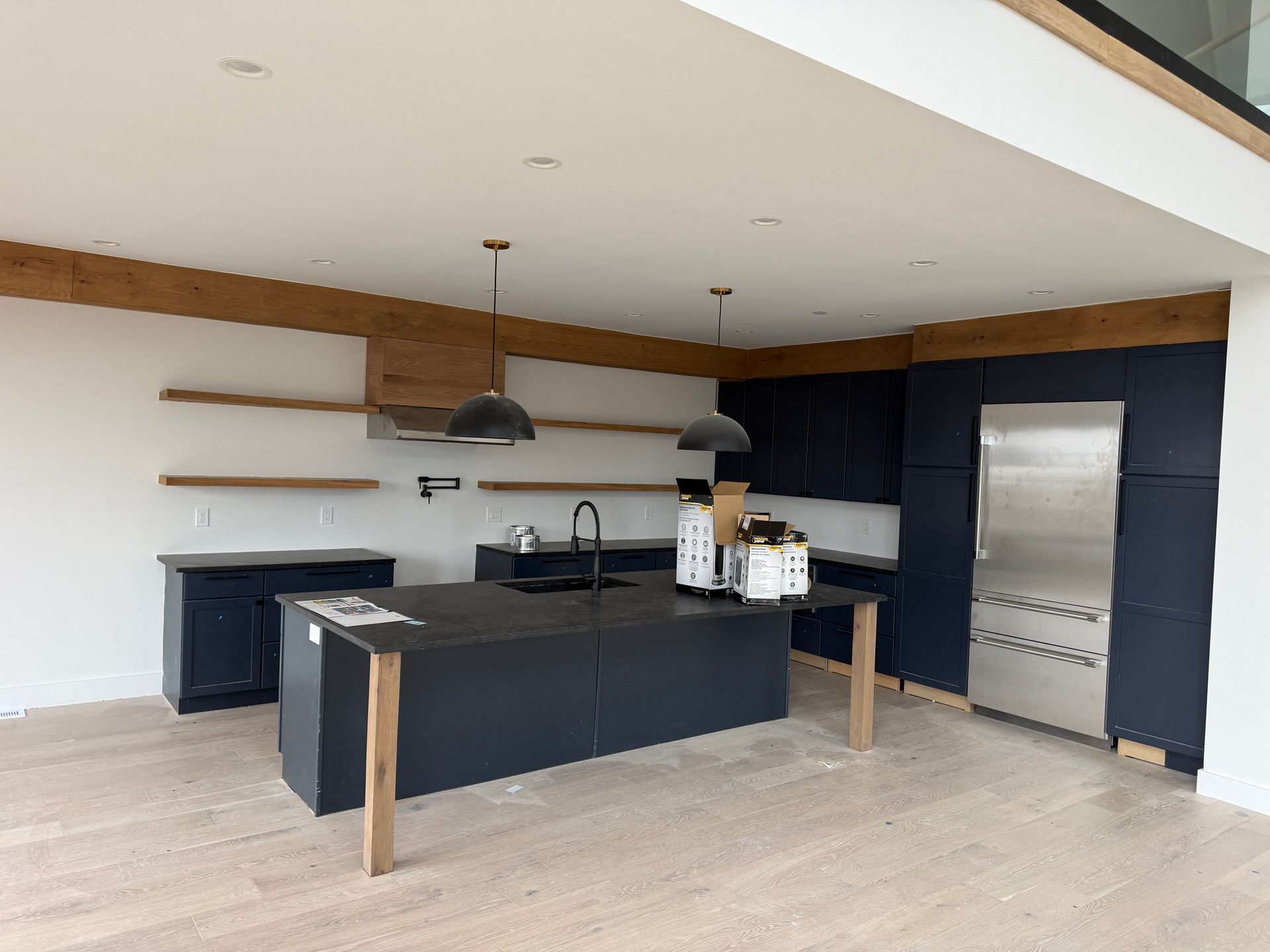 A modern kitchen with navy blue cabinetry, a dark island, light wood floating shelves, and a large stainless refrigerator.
