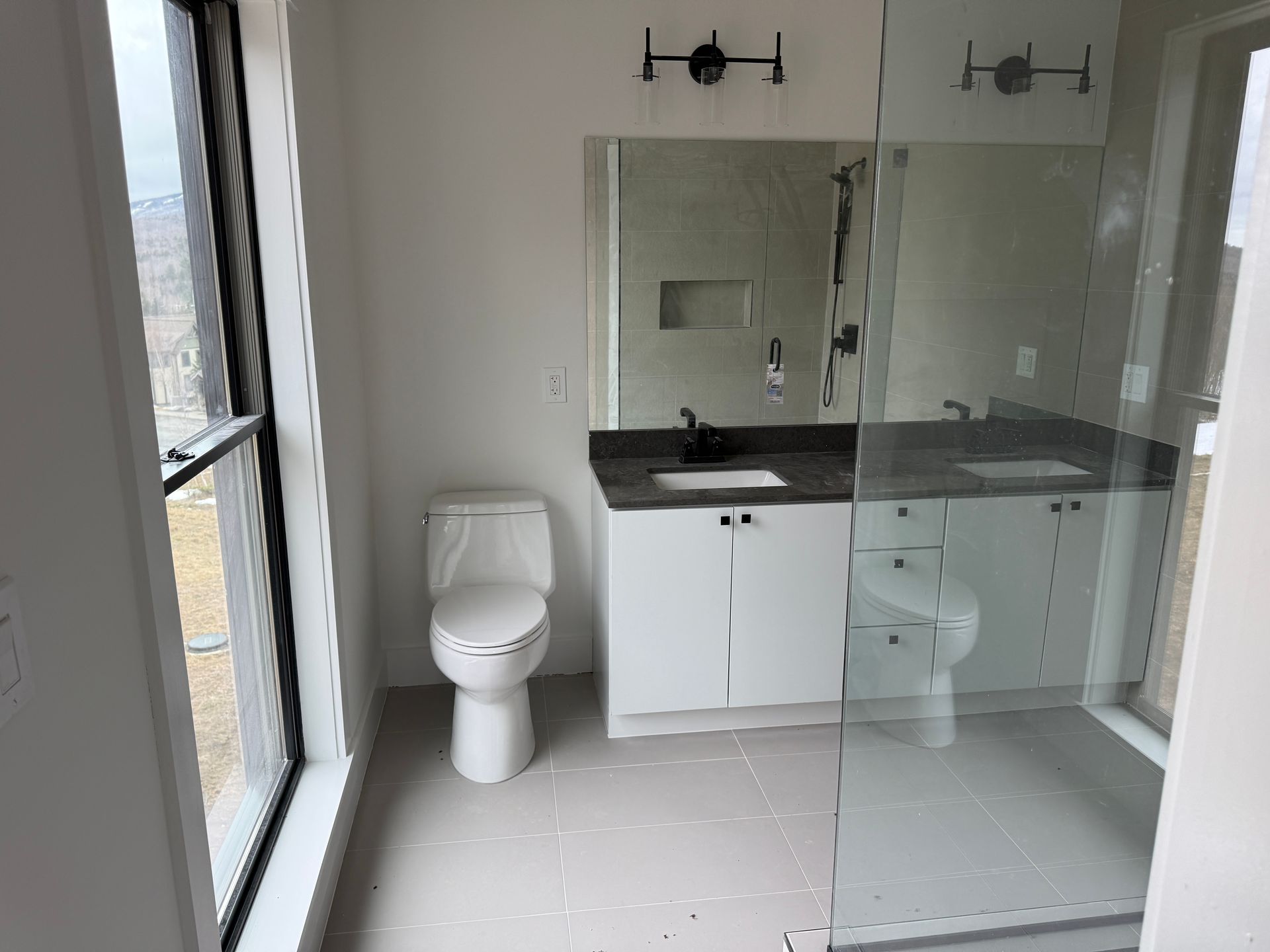 A modern bathroom featuring a white toilet, a white vanity with a dark countertop, and a glass-enclosed shower.