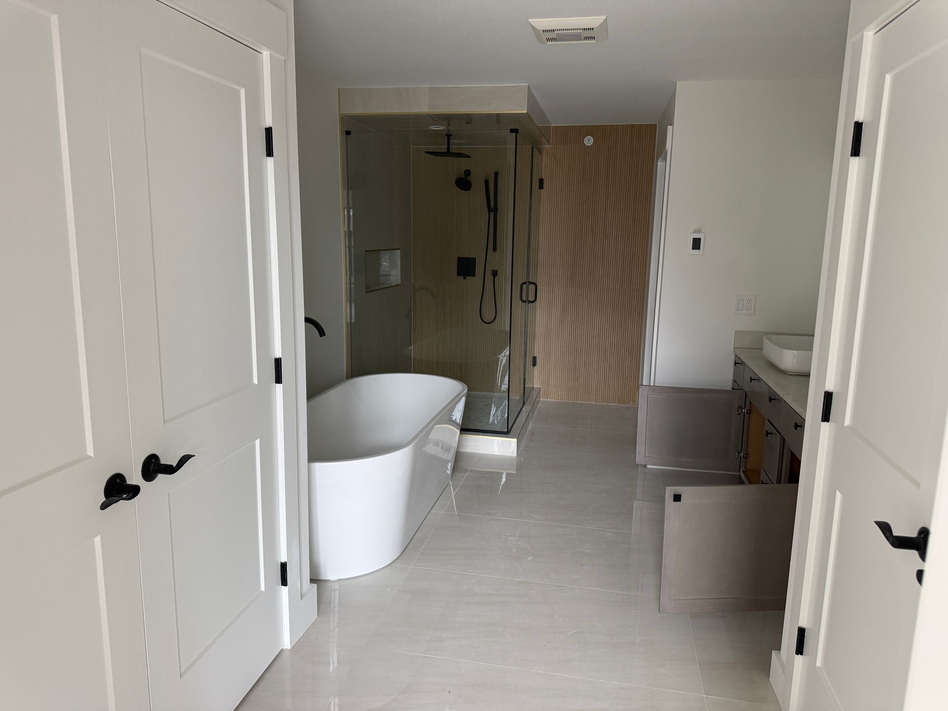 A modern bathroom featuring a white freestanding tub, a glass-enclosed shower, and a wooden vanity on a tiled floor.
