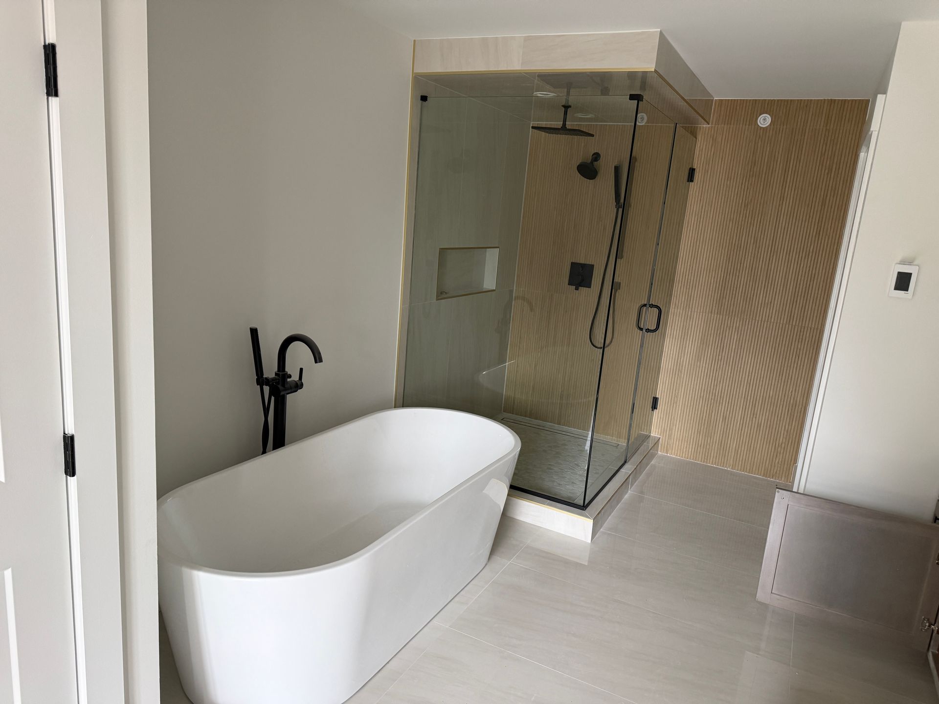 A modern bathroom featuring a white freestanding bathtub with black fixtures next to a glass-enclosed shower.