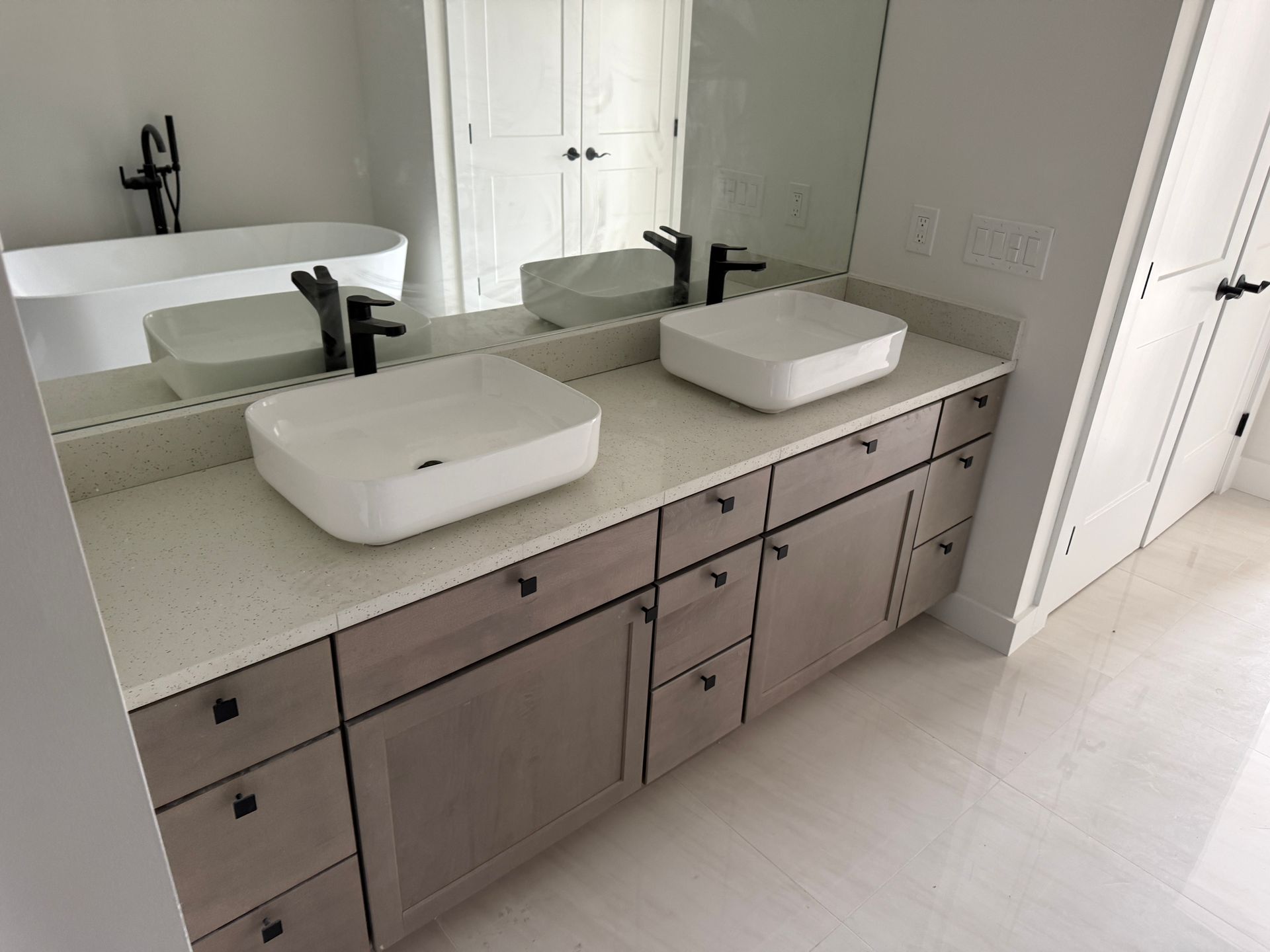 Modern bathroom with a double vanity, vessel sinks, black fixtures, and a freestanding tub in a light-toned room.