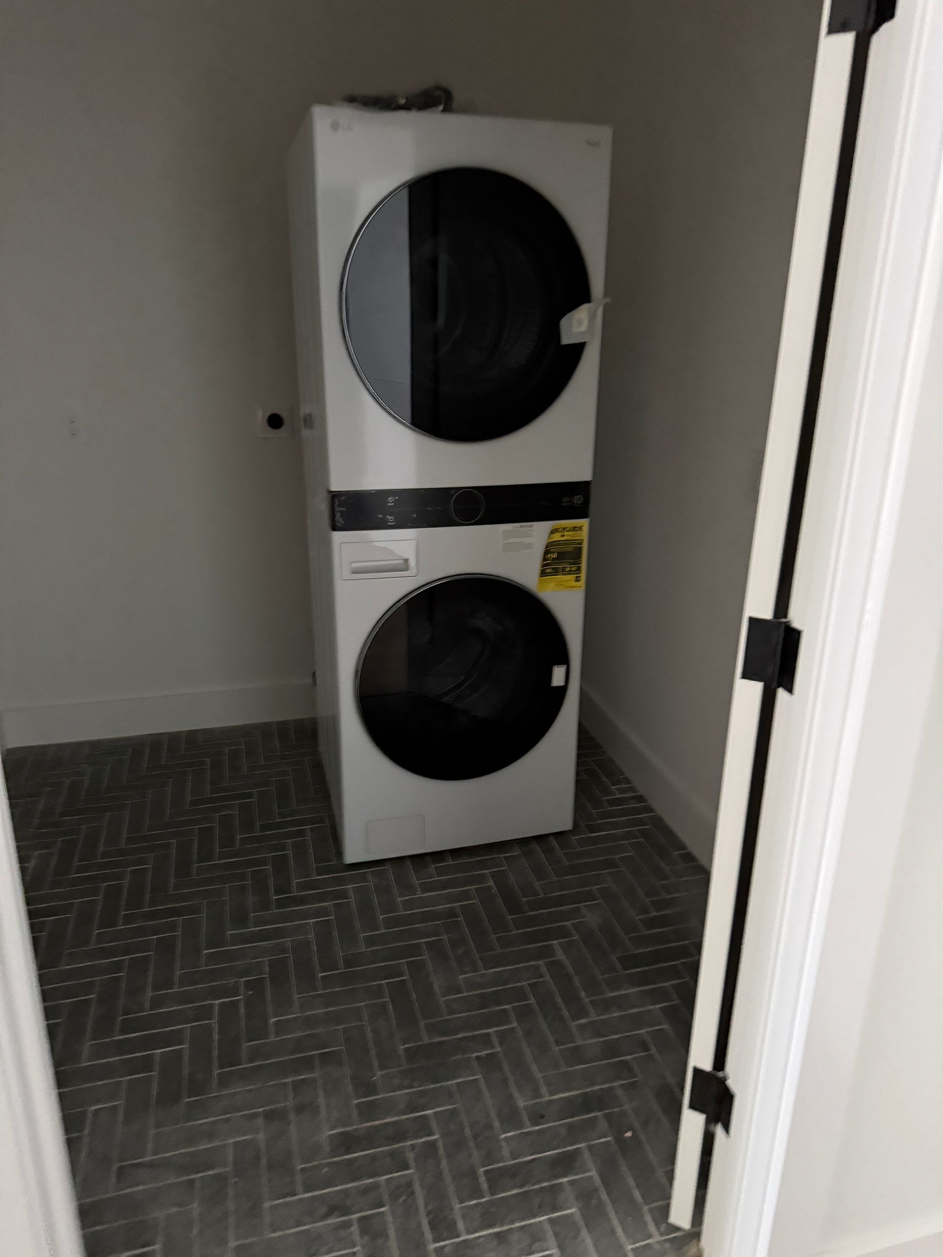 White stacked washer and dryer unit located in a small, tiled laundry closet.