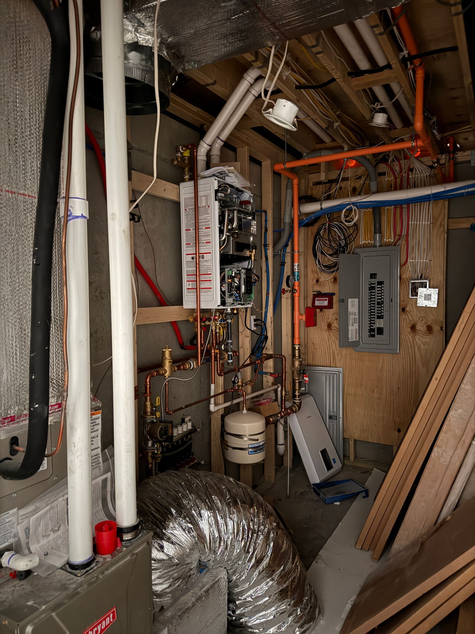 Mechanical room with a tankless water heater, white PVC pipes, copper plumbing, electrical panel, and HVAC equipment.