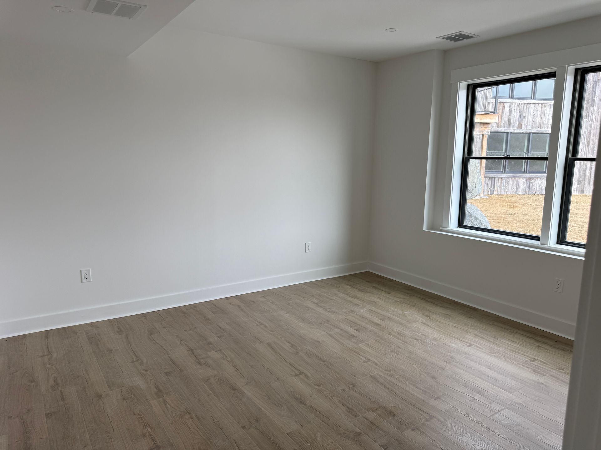 A vacant room with white walls, light wood flooring, and a large window looking out onto a construction site.