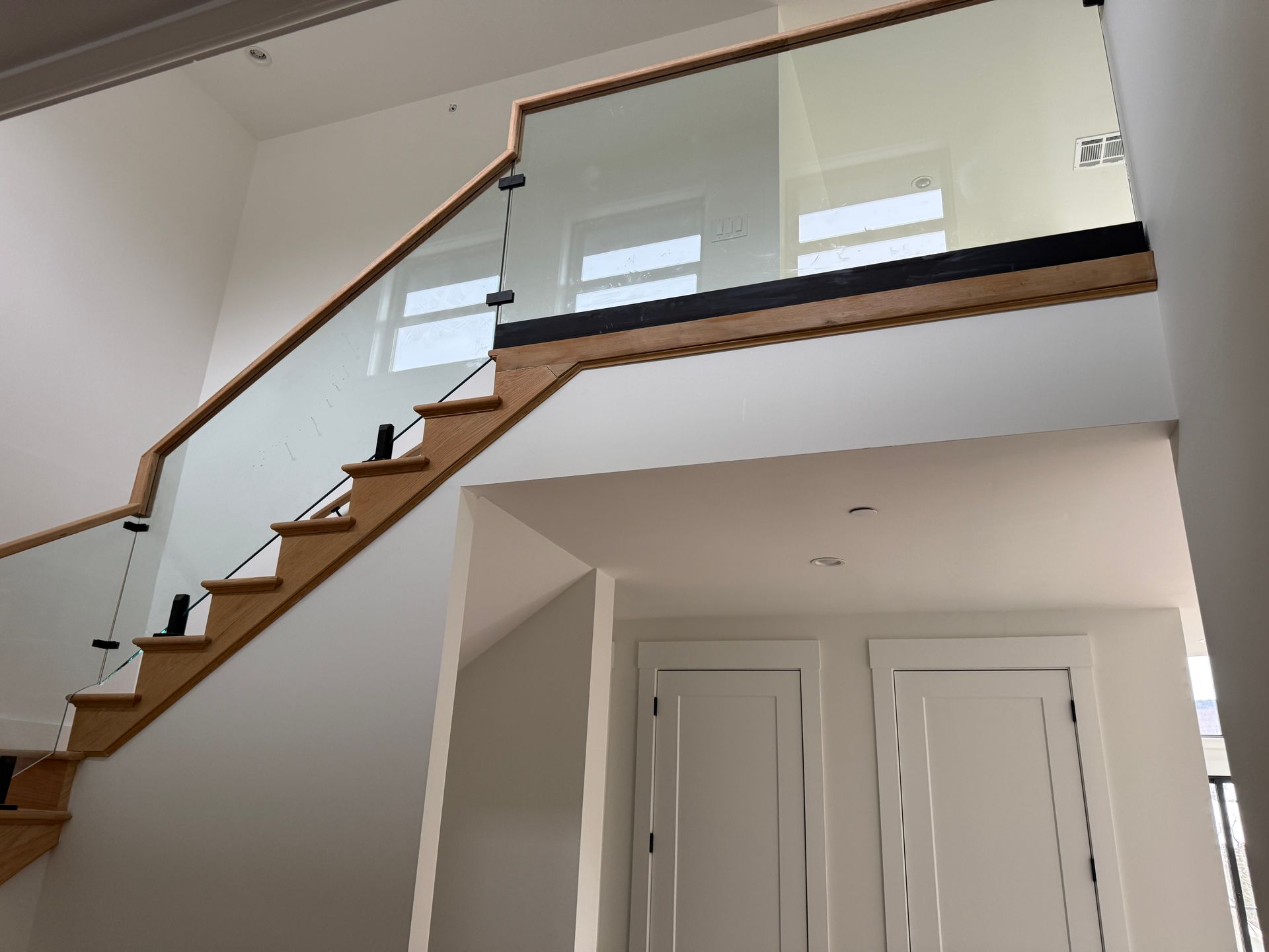 A wooden staircase with a glass railing and metal clamps, leading to an upper level next to two white doors.