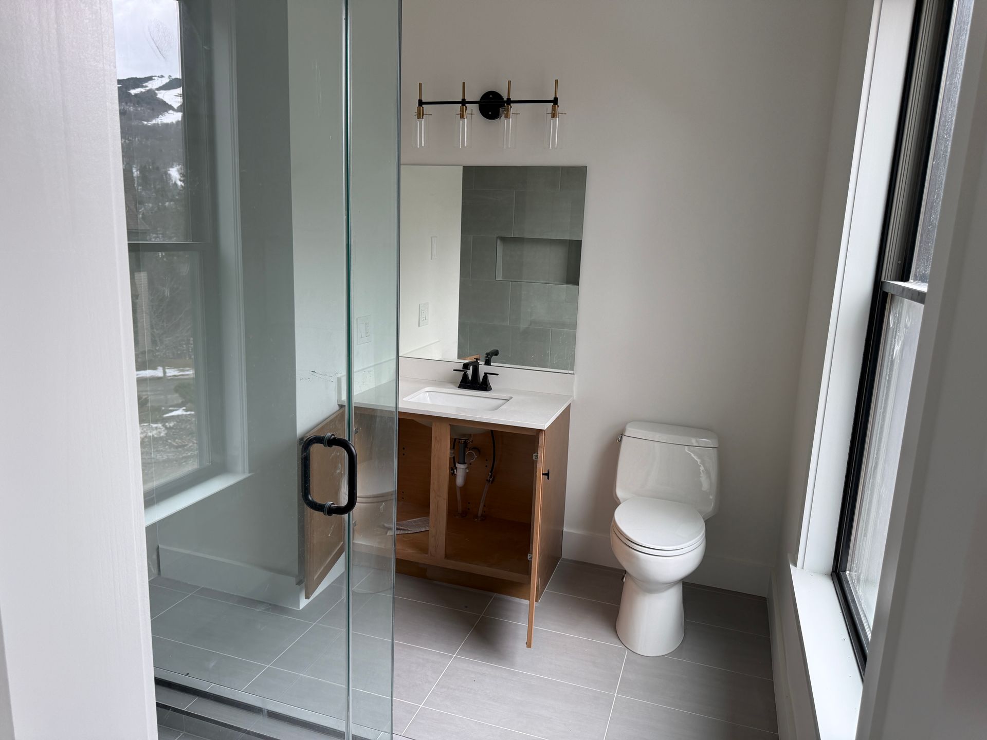 A modern bathroom featuring a glass-enclosed shower, a vanity with a white countertop, and a white toilet on grey tile.