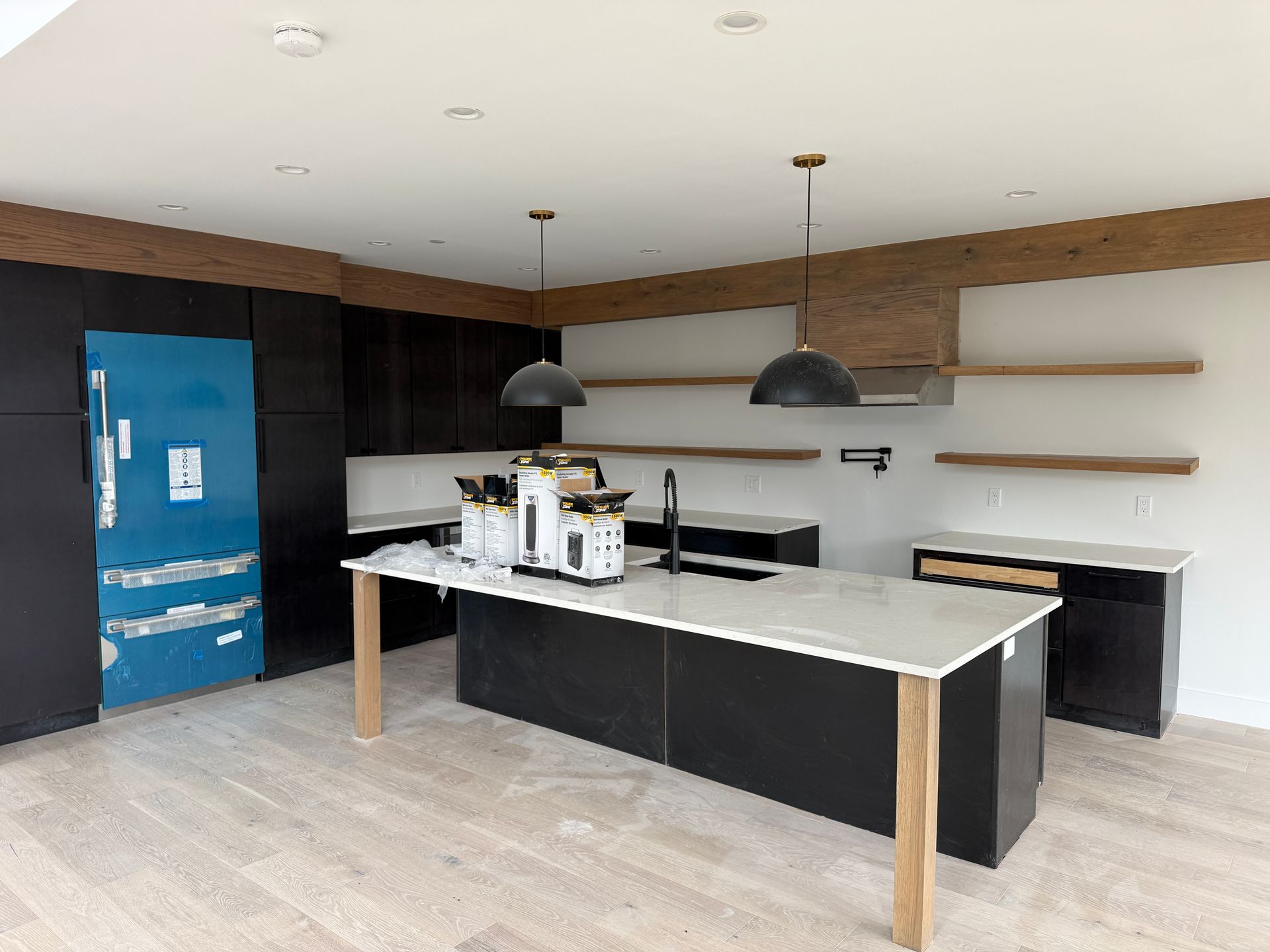 Modern kitchen with black cabinets, a white island, wooden shelves, and a blue-covered refrigerator.