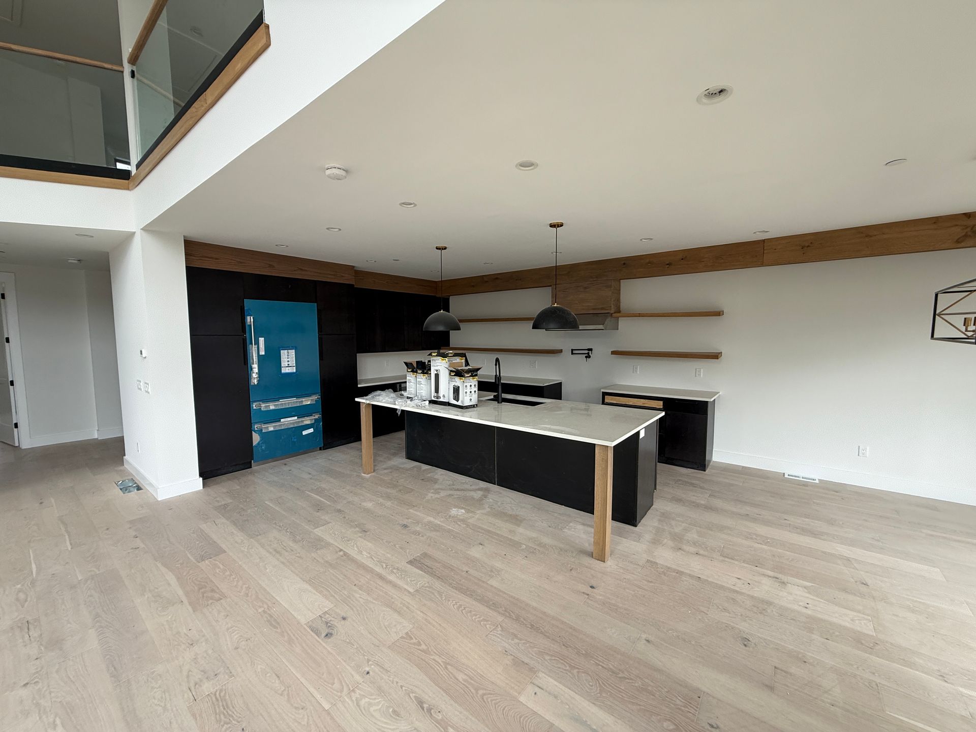 A modern kitchen featuring a dark island, light wood flooring, open shelving, and a refrigerator covered in blue plastic.