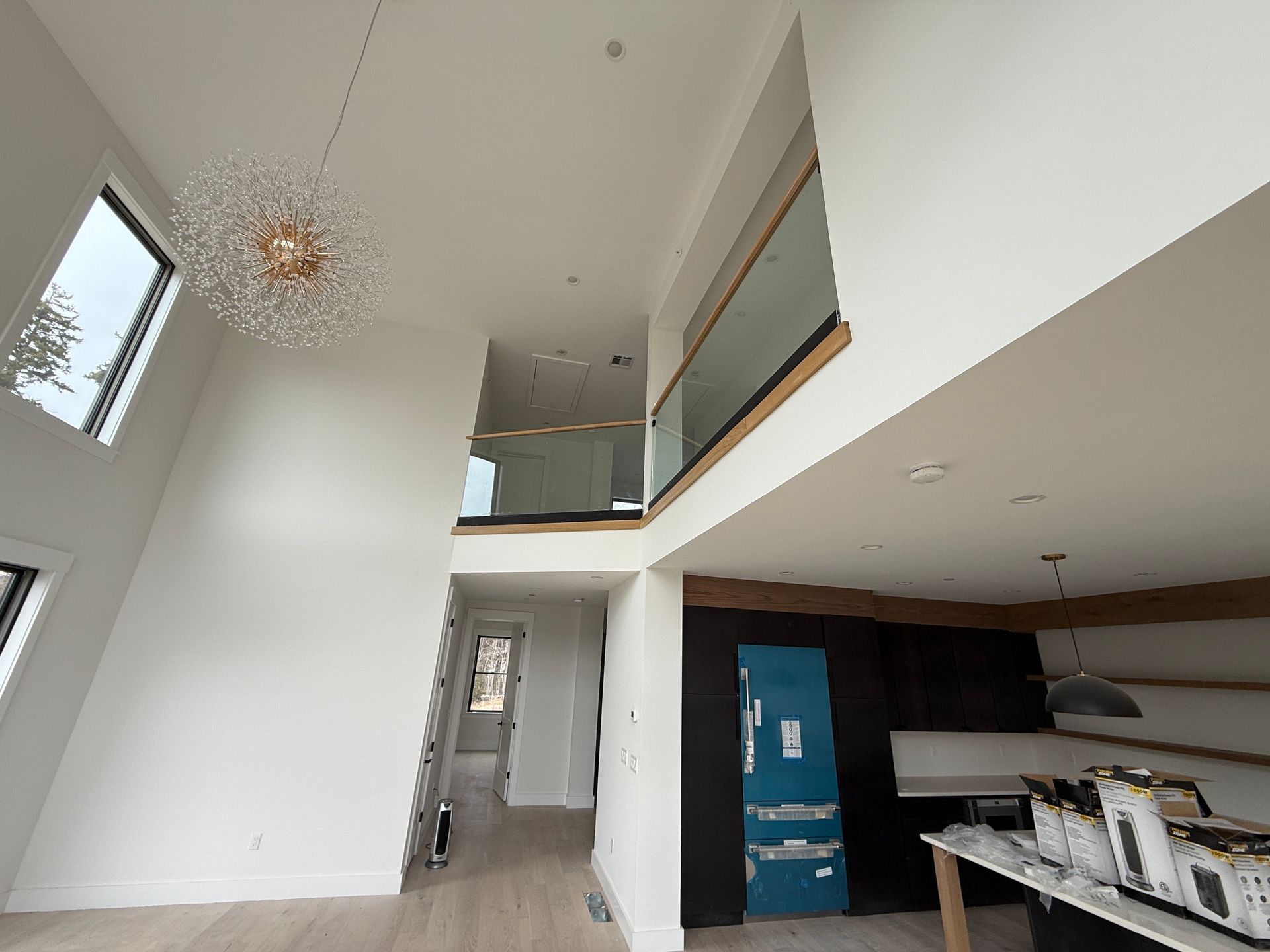Modern home interior with high ceilings, a crystal chandelier, a glass-railed loft, and an open-concept kitchen area.