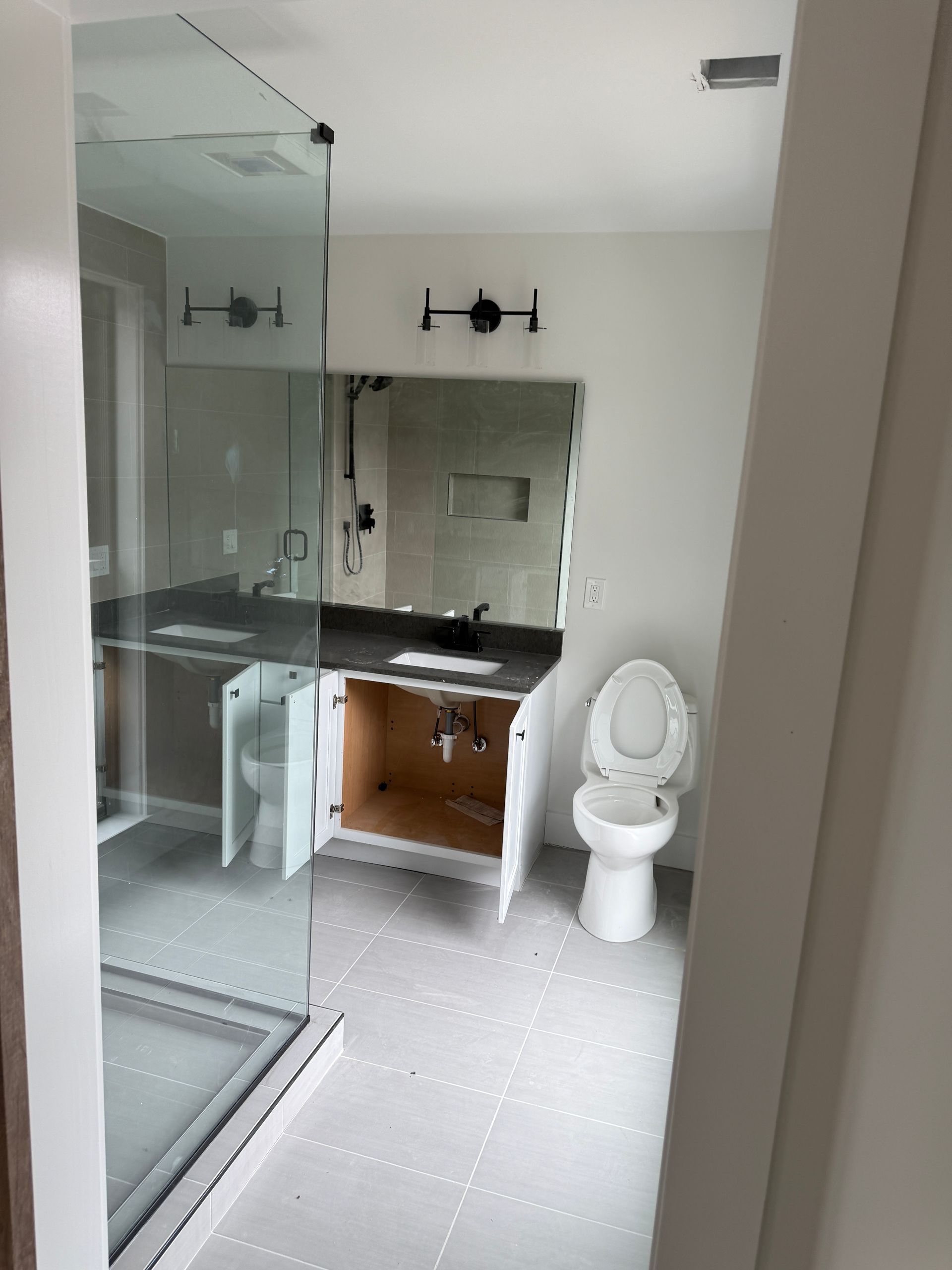 A partially renovated bathroom featuring a glass-enclosed shower, a vanity without doors, a mirror, and a white toilet.