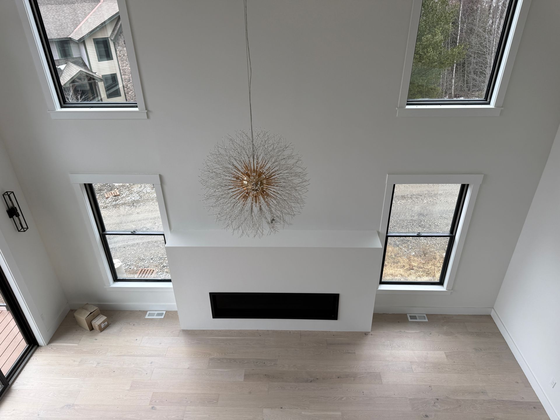 High-angle view of a modern living room featuring a linear fireplace, light wood floors, and a sputnik chandelier.