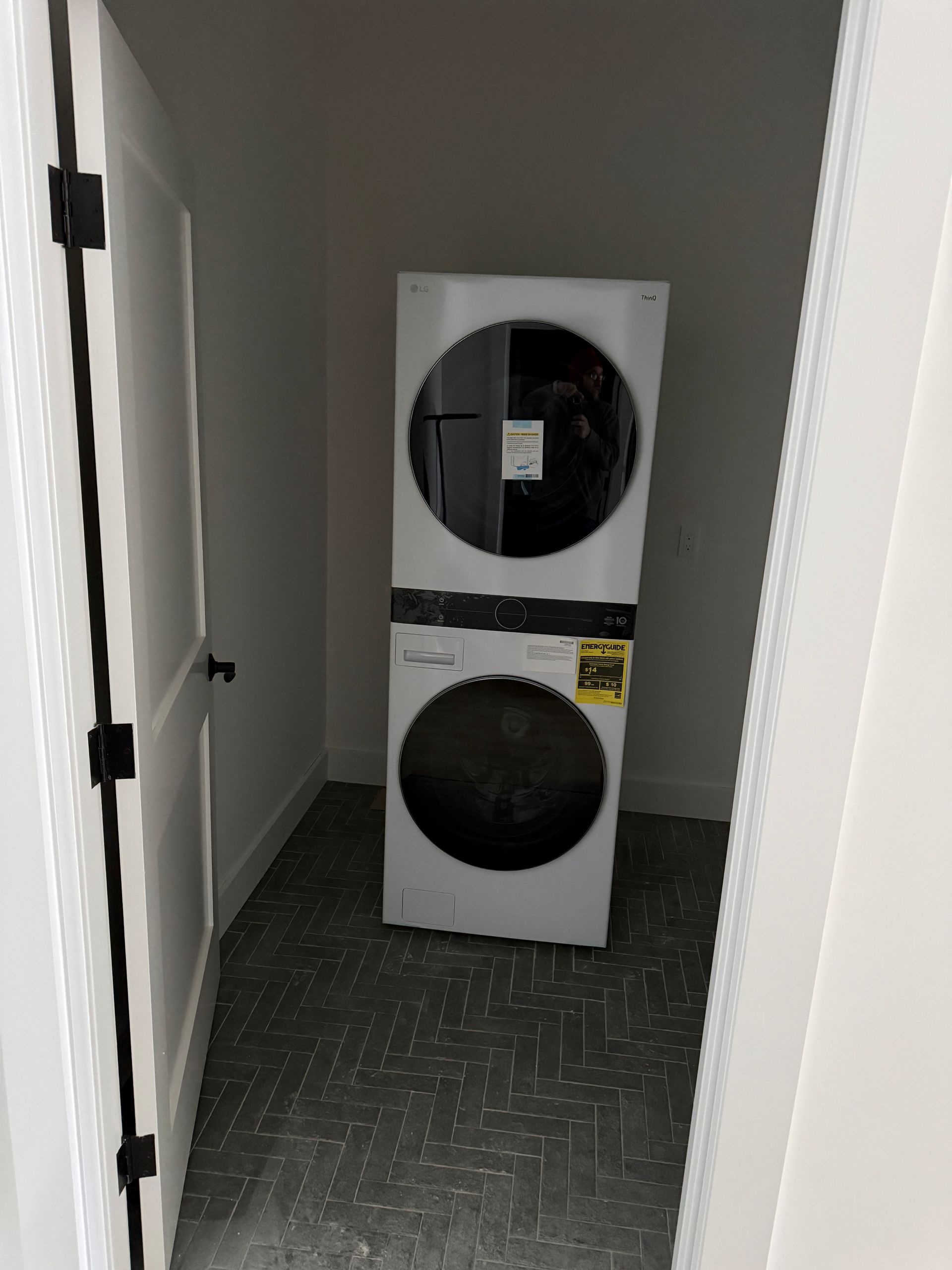 A white stacked washer and dryer unit stands in a small, empty closet with a gray floor and white walls.