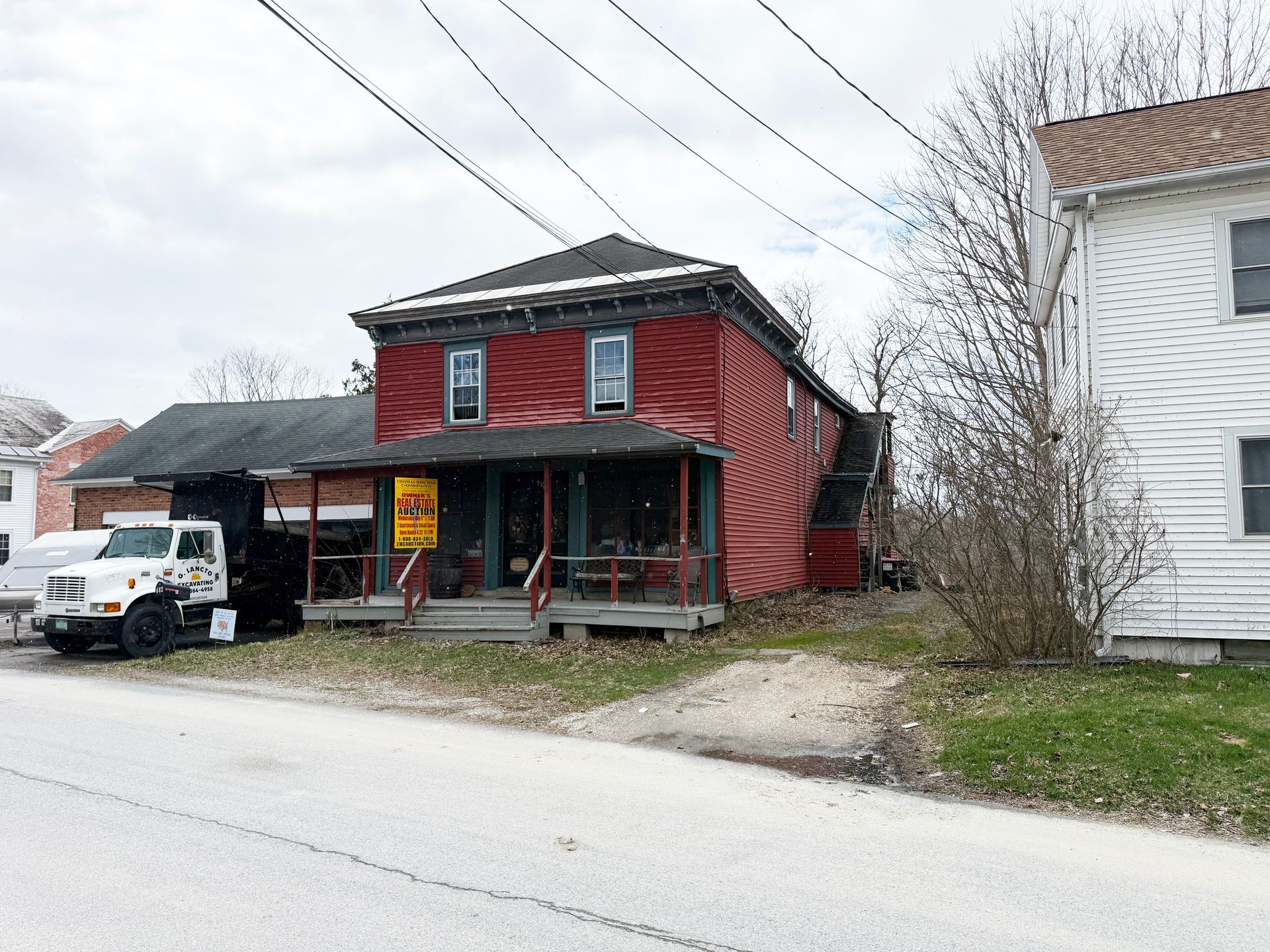 A red, two-story house with a front porch sits next to a white house.