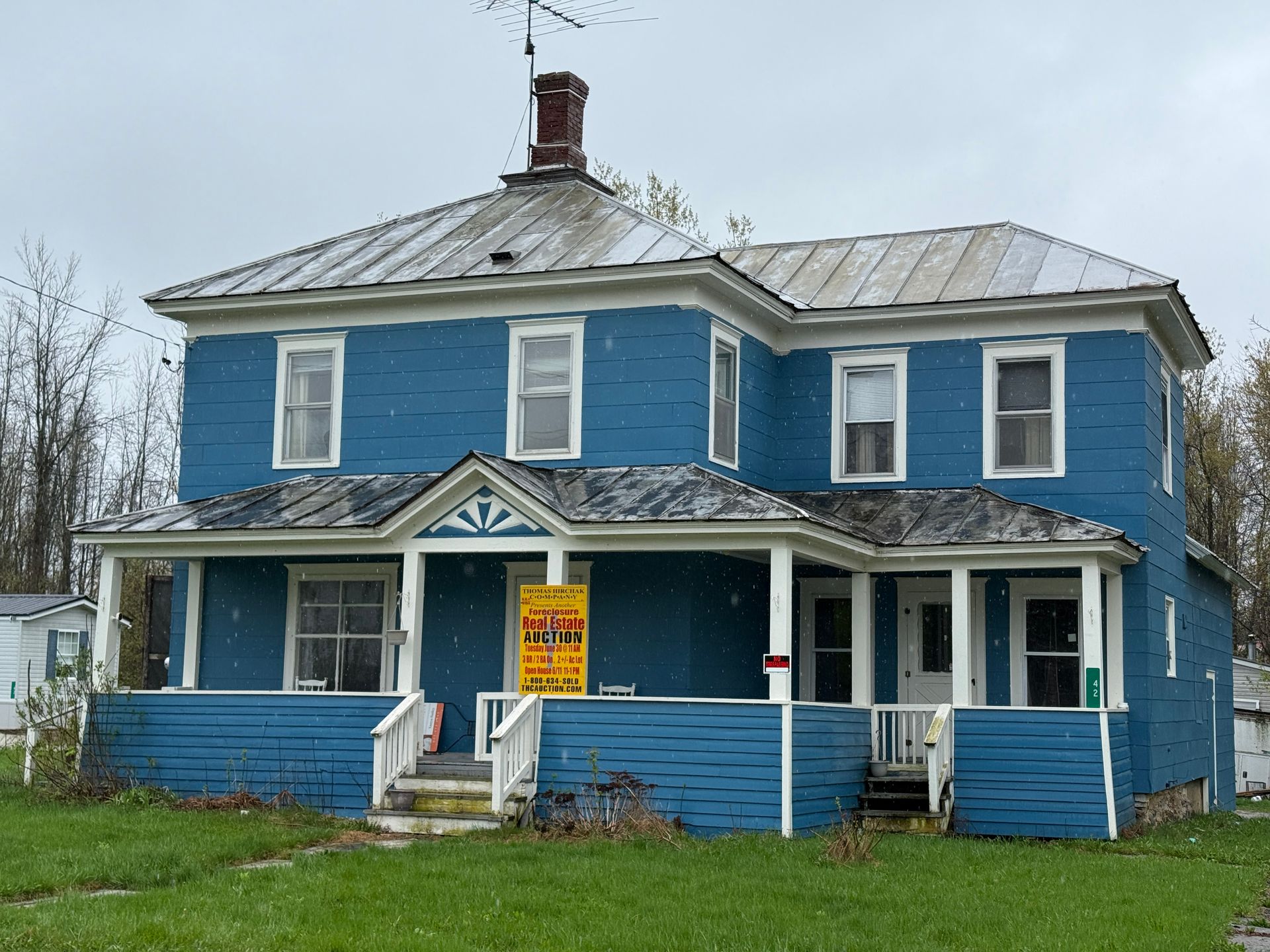 Blue two-story house with a porch and a yellow for-sale sign in the front yard
