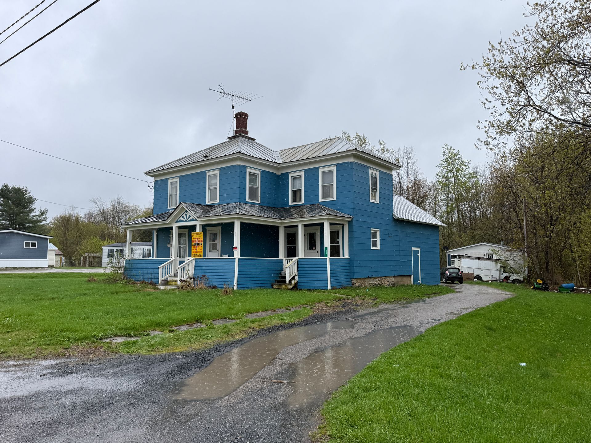Blue two-story house with white trim beside a driveway on a cloudy day