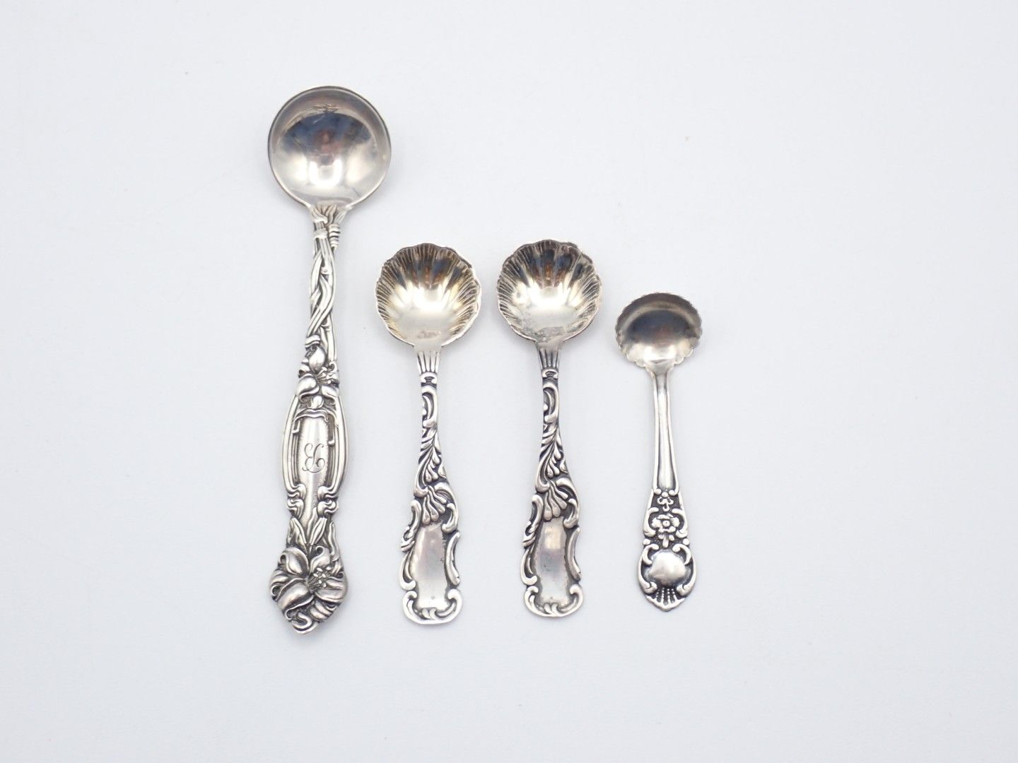 Four ornate silver teaspoons arranged by size on a white background