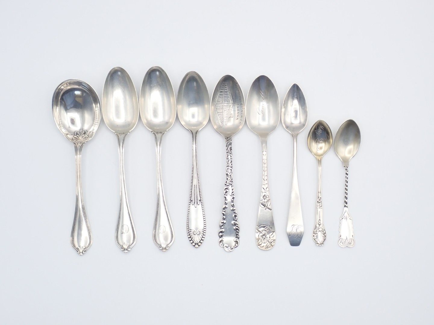 Set of silver antique-style spoons and serving utensils on a white background