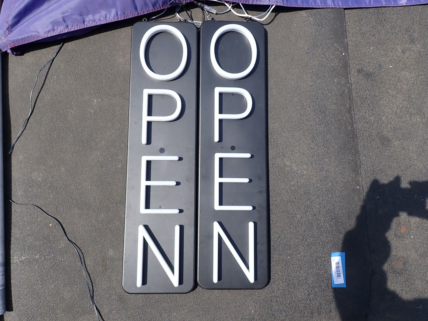 Two vertical black signs on a sidewalk spelling “OPEN” in white letters.