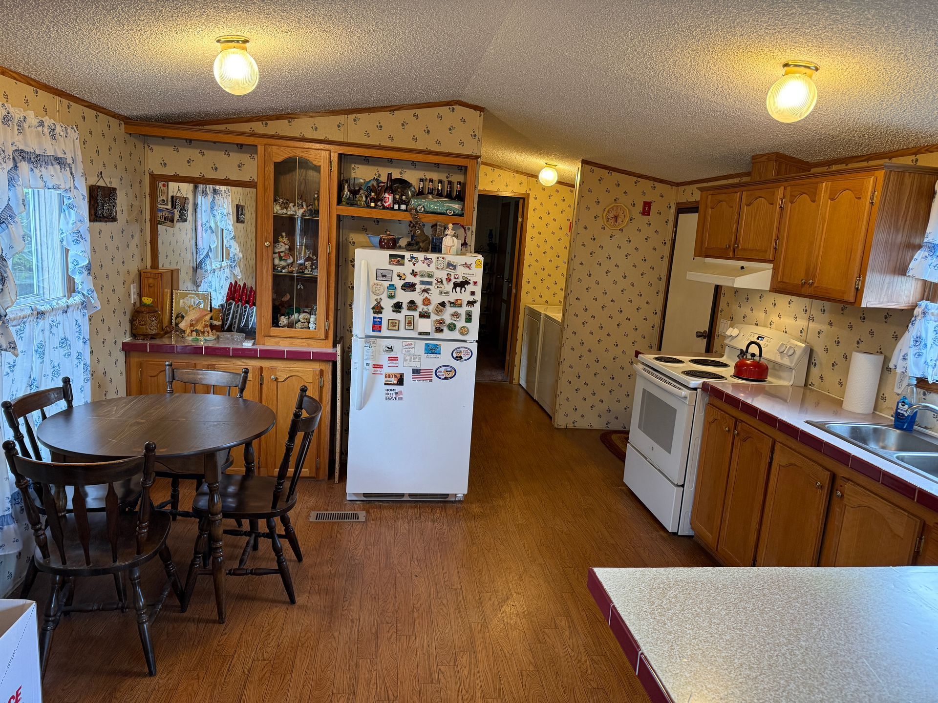 Wide kitchen with wooden cabinets, white appliances, dining table, and a refrigerator covered in magnets.