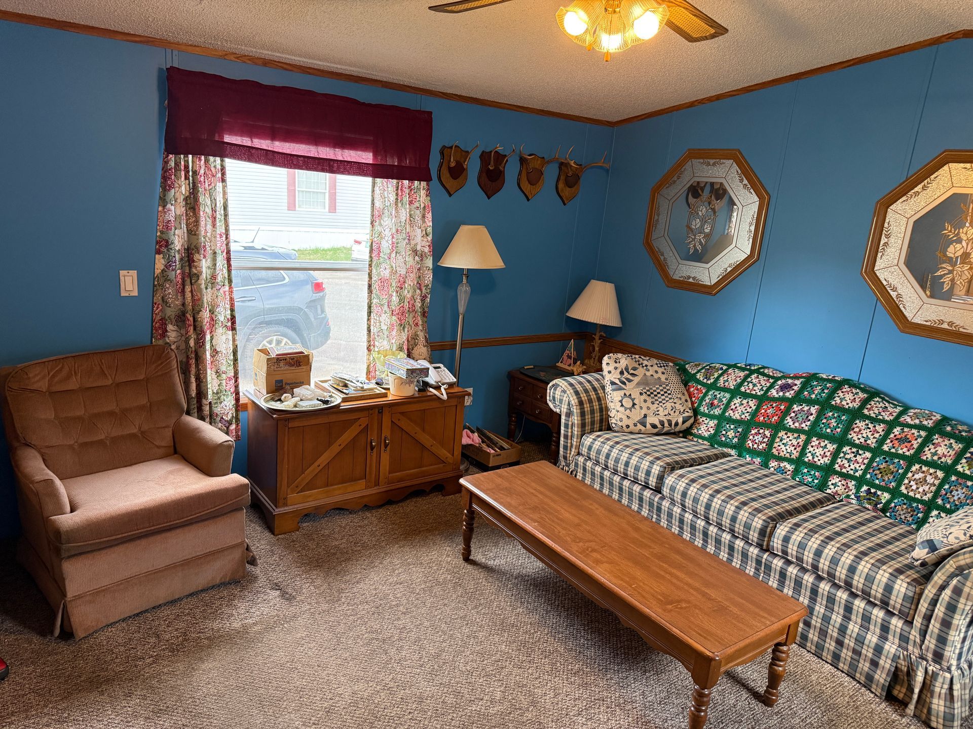 Blue living room with sofa, armchair, coffee table, window, lamps, and wall mirrors