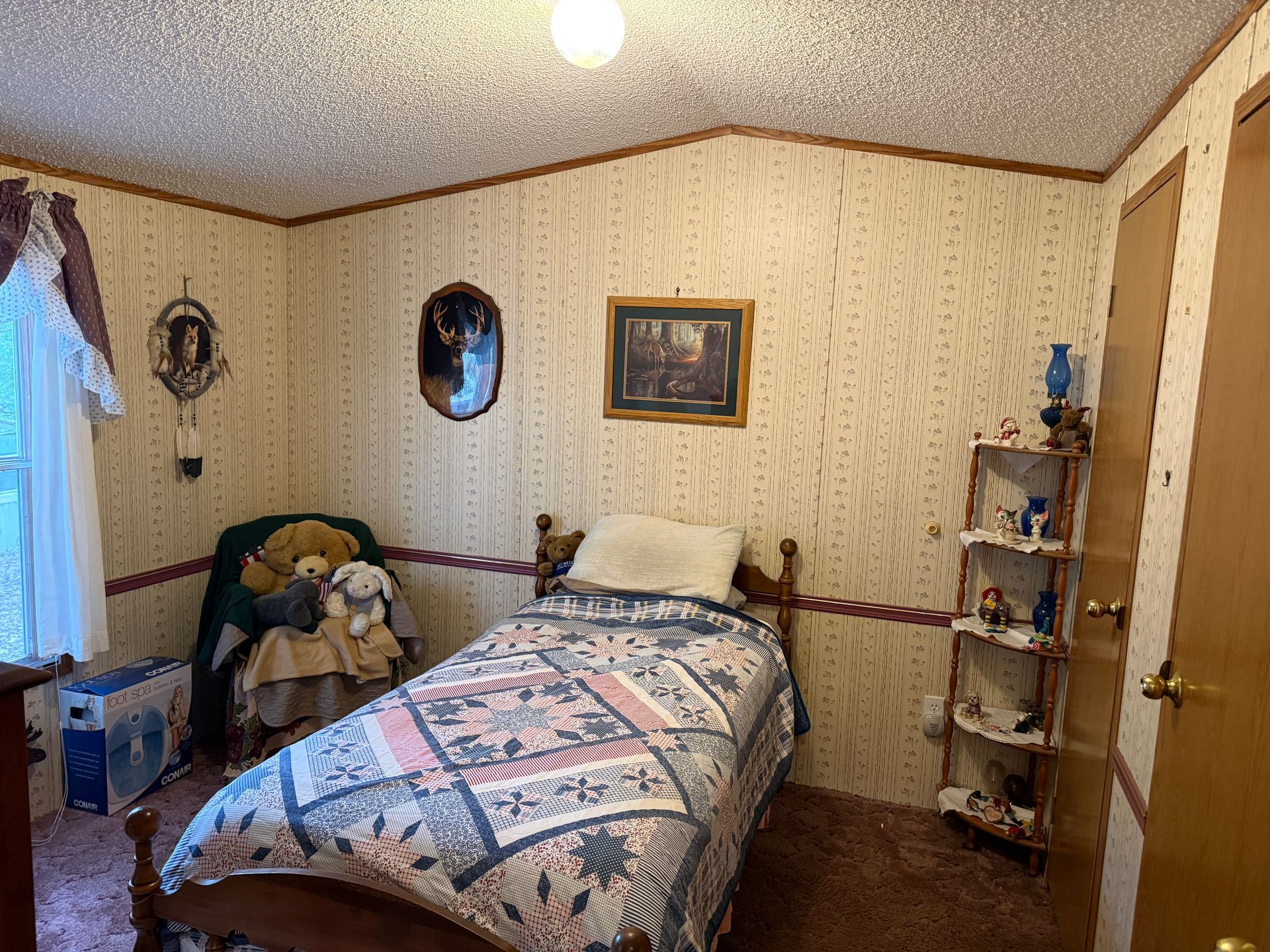Small bedroom with a bed, quilt, chair, wall decor, and a small shelving unit.