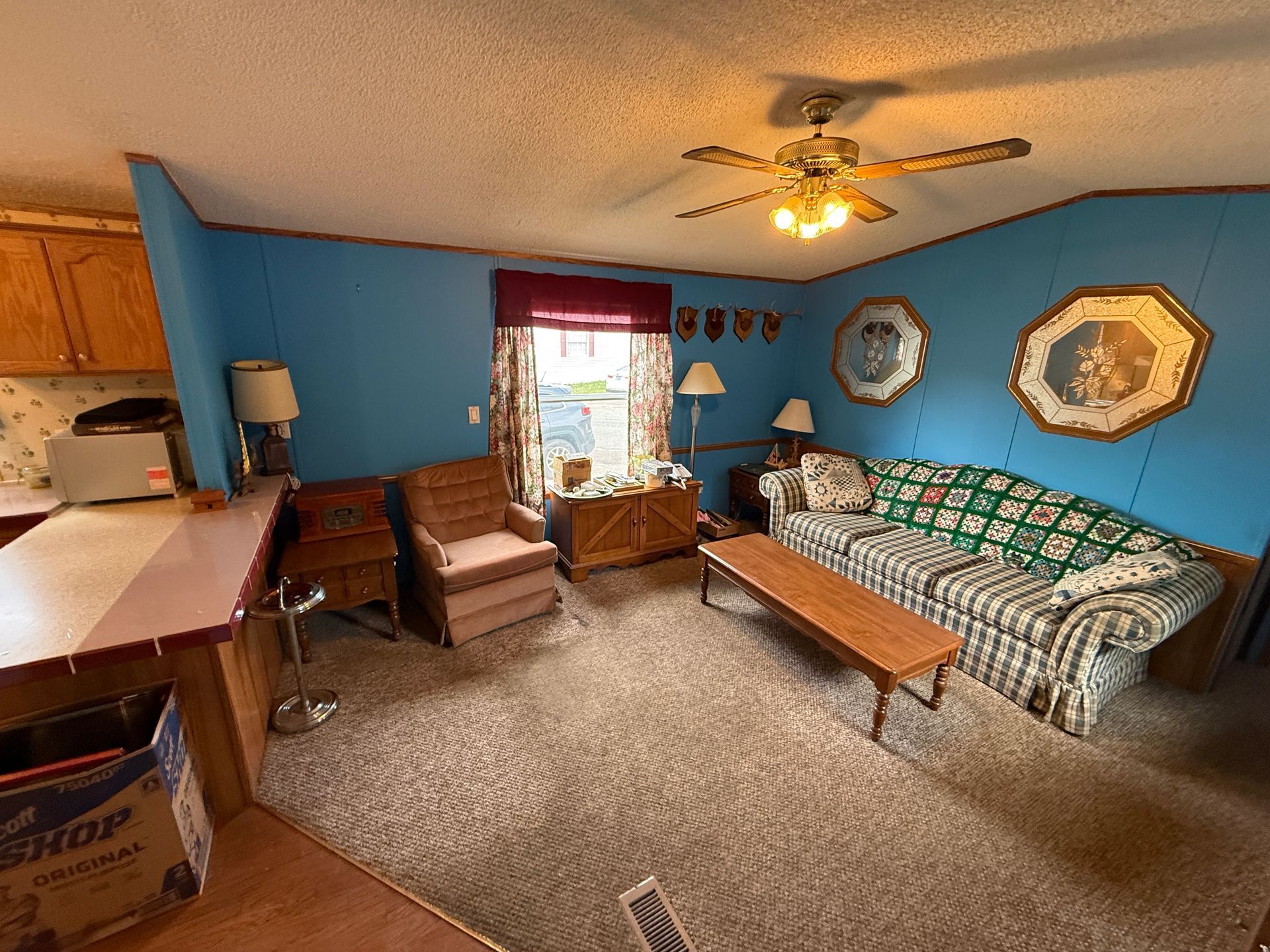 Cozy living room with blue walls, patterned sofa, armchair, coffee table, and ceiling fan by a window