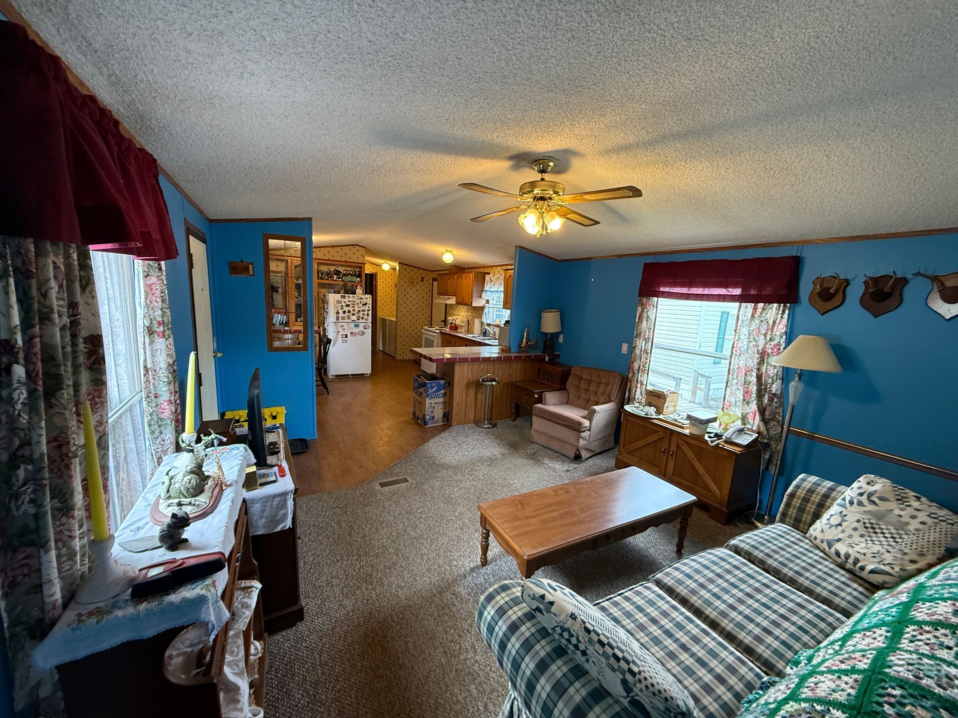 Cozy blue living room with sofa, coffee table, windows, and a ceiling fan opening to a dining area